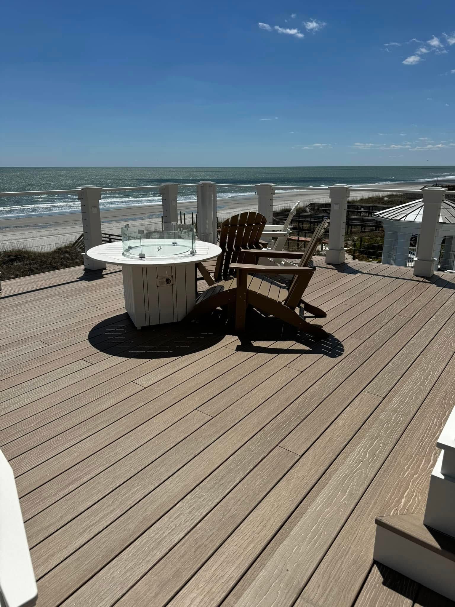 Oceanfront deck with white chairs and table overlooking the beach and waves under a clear blue sky