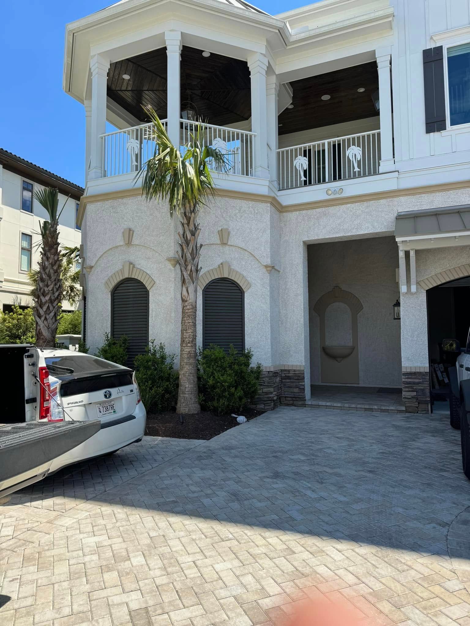 White two-story house with arched entry, balcony, and a car parked in the driveway.