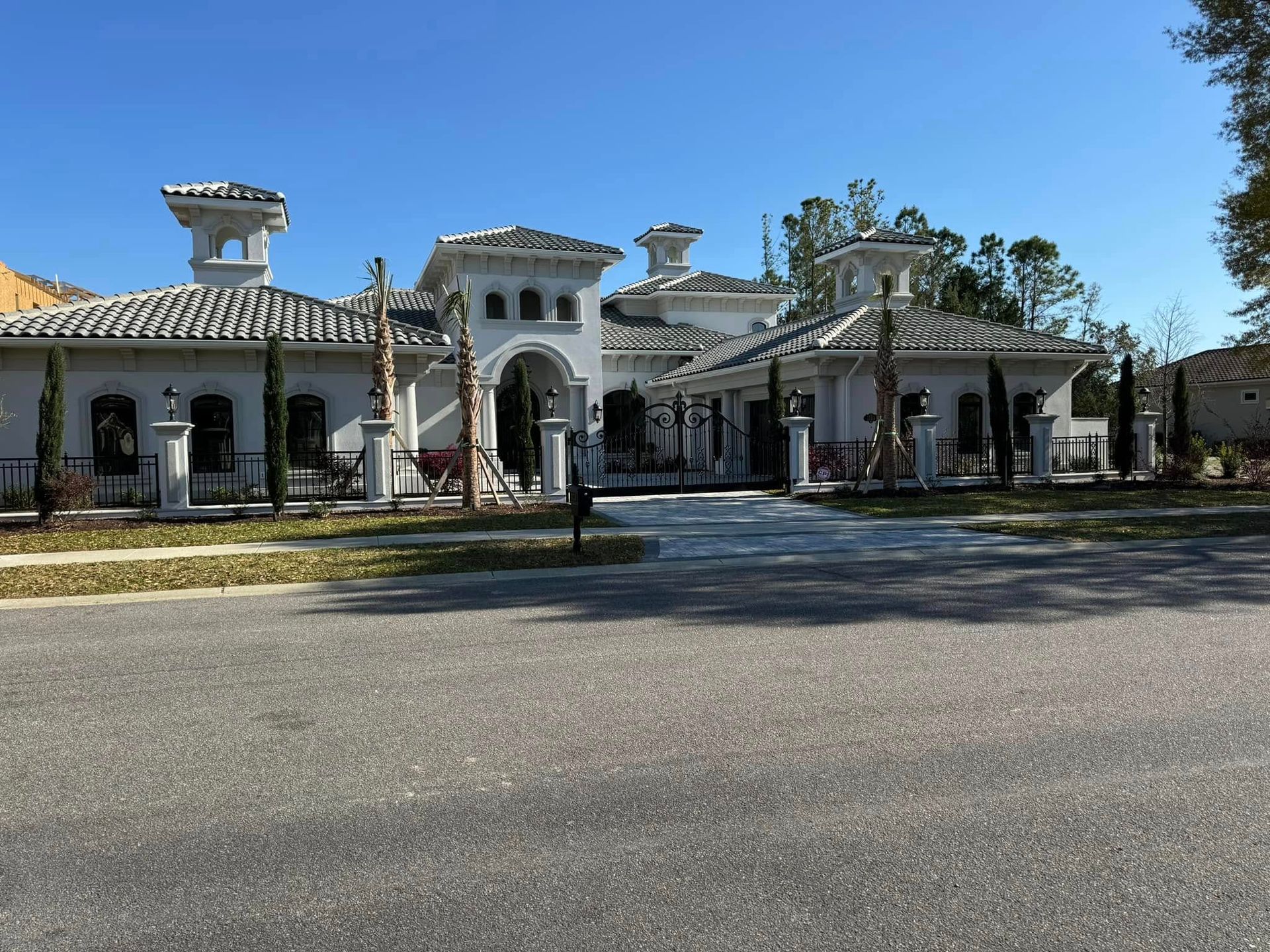 Grand white villa with arched entrance, terracotta roof, and fountain in front under a clear blue sky