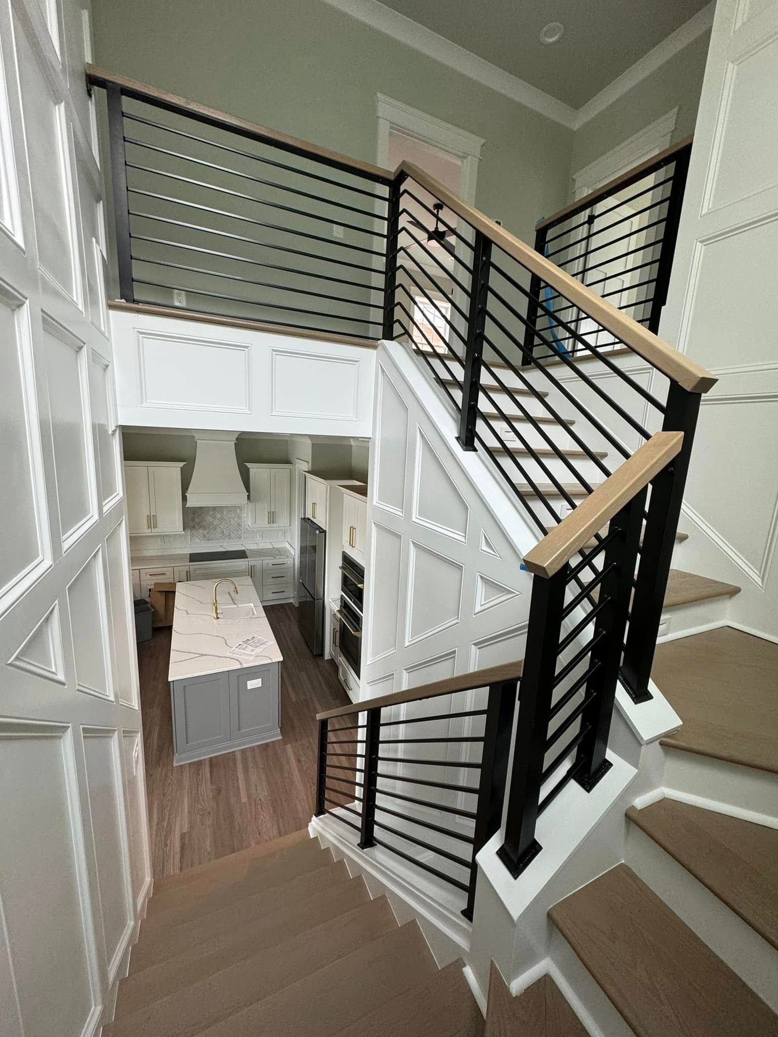 Interior view of a modern staircase overlooking a kitchen, with black railings and white walls