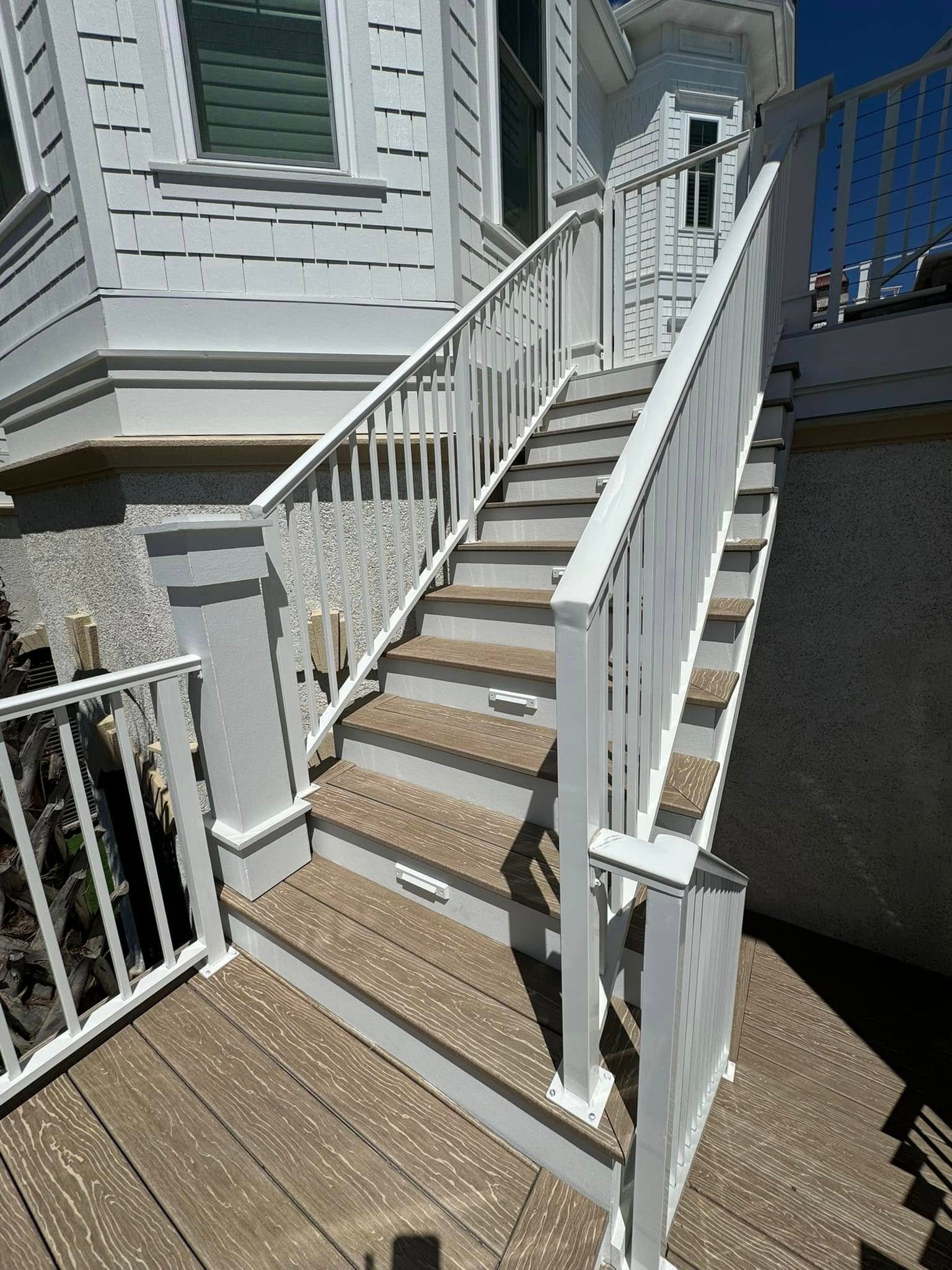 Outdoor wooden staircase with white railings leading up to a house deck