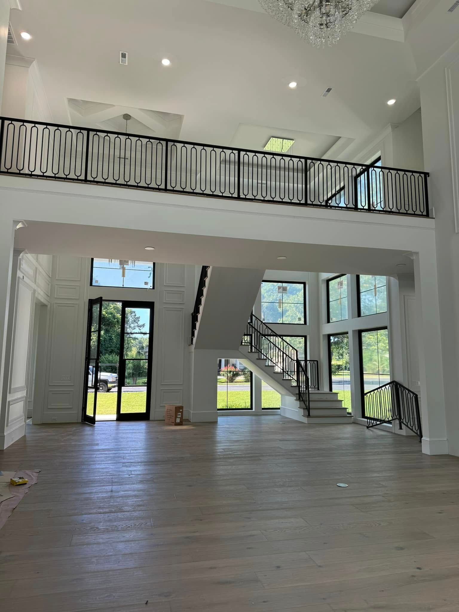 Spacious modern living room with white walls, high ceiling, staircase, and large windows overlooking a yard