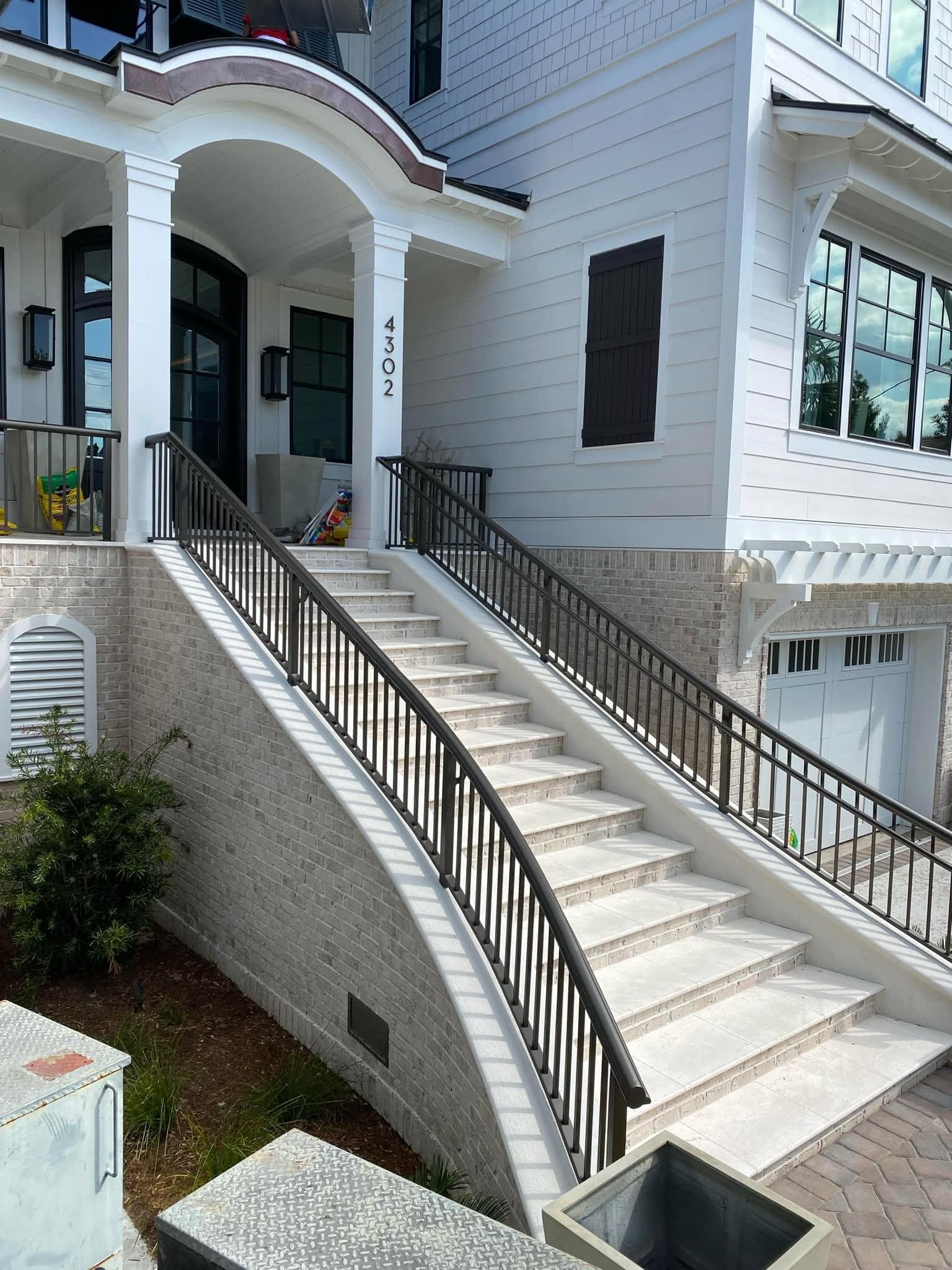 White townhouse entrance with twin staircases, black railings, and arched porch under bright daylight