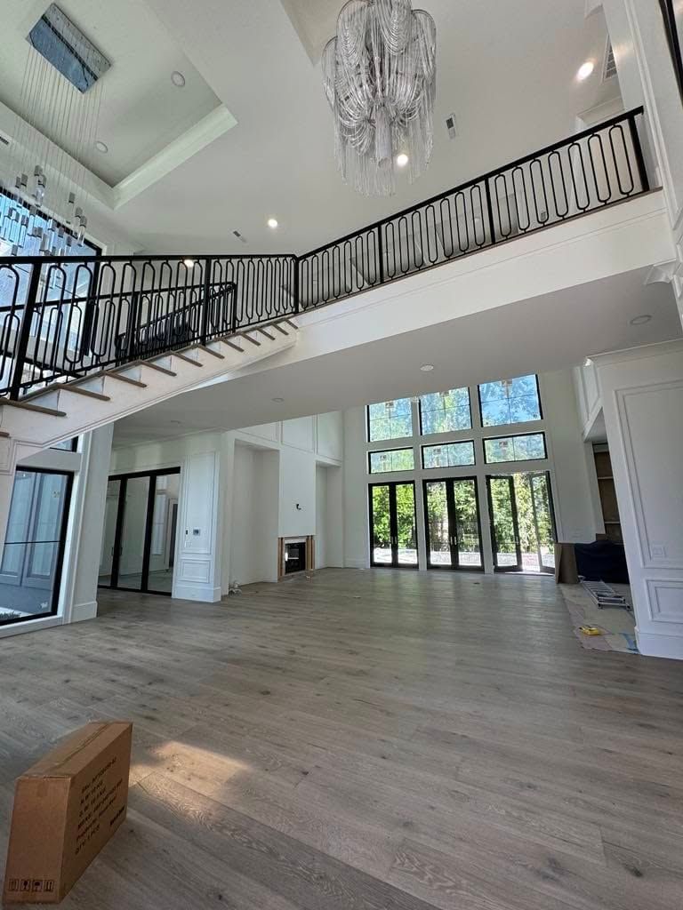 Bright modern living room with high ceilings, staircase, chandelier, and large windows overlooking trees