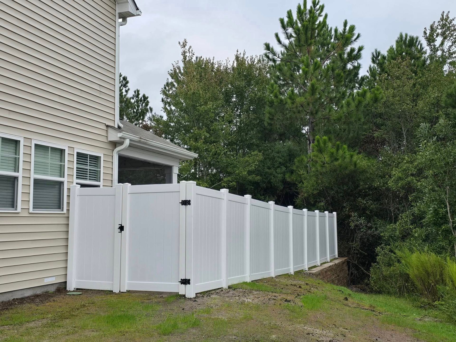 White vinyl privacy fence beside a beige house, running along a grassy yard with trees in the background