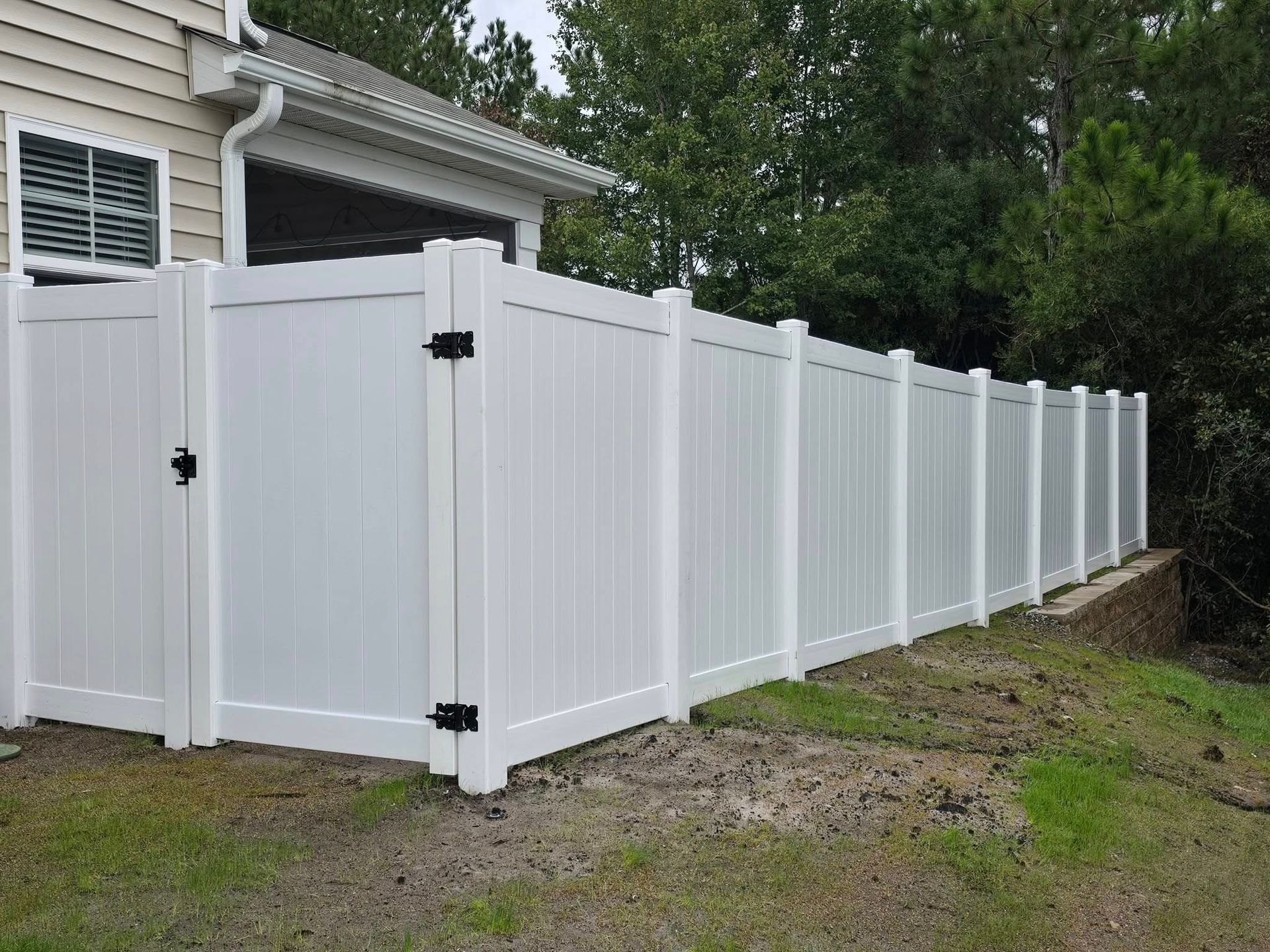 White vinyl privacy fence with gate beside a house, running along a gravel yard.
