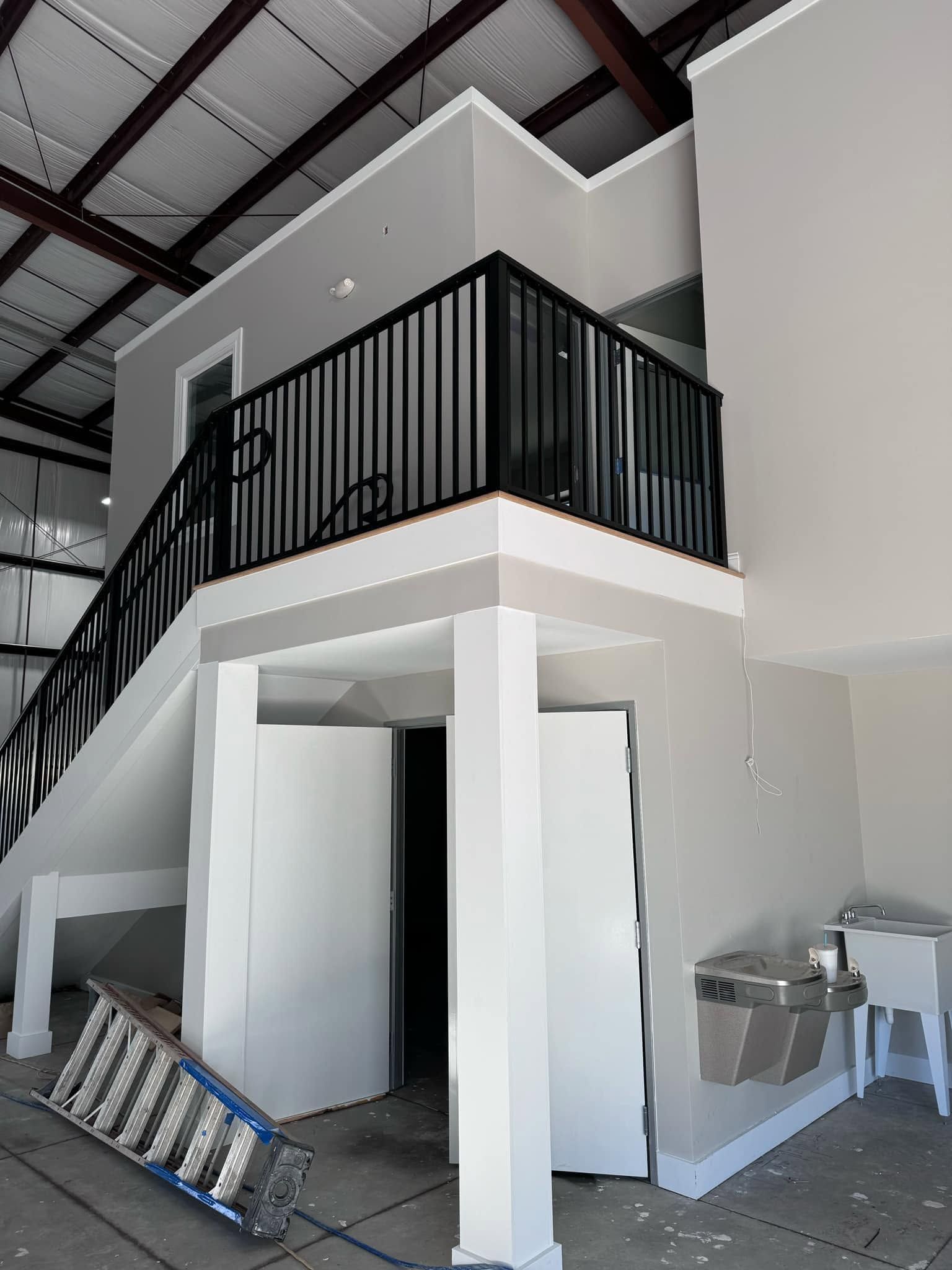 Interior stairwell with black railing, white walls, and trash bins on the lower level