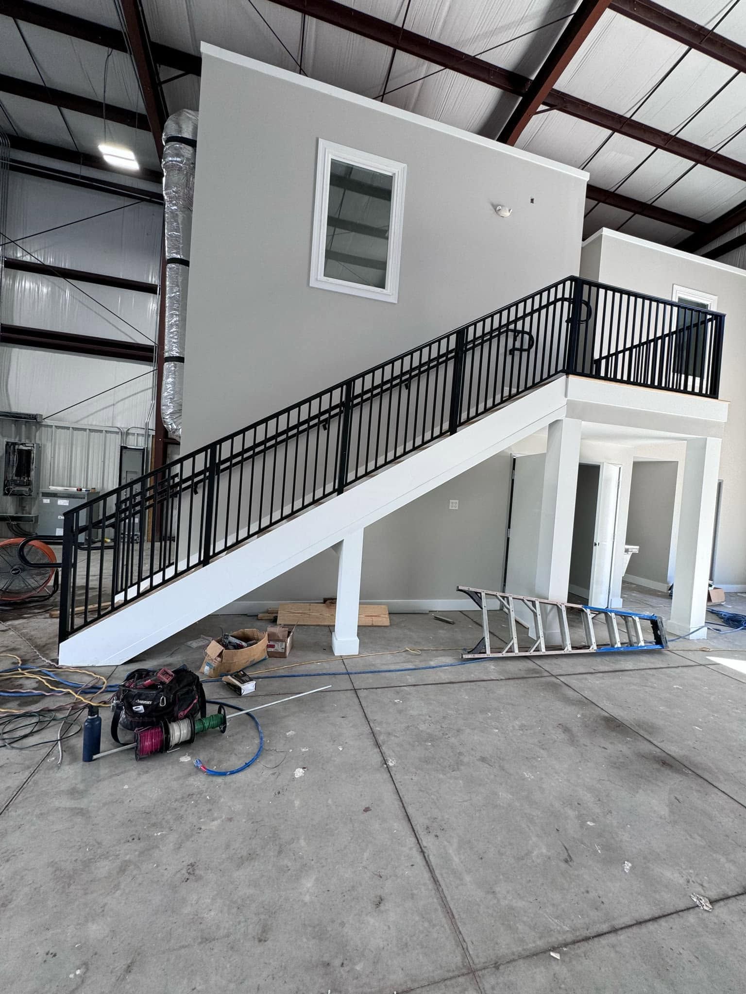 Small white modular building with exterior staircase inside a warehouse, construction materials scattered nearby.