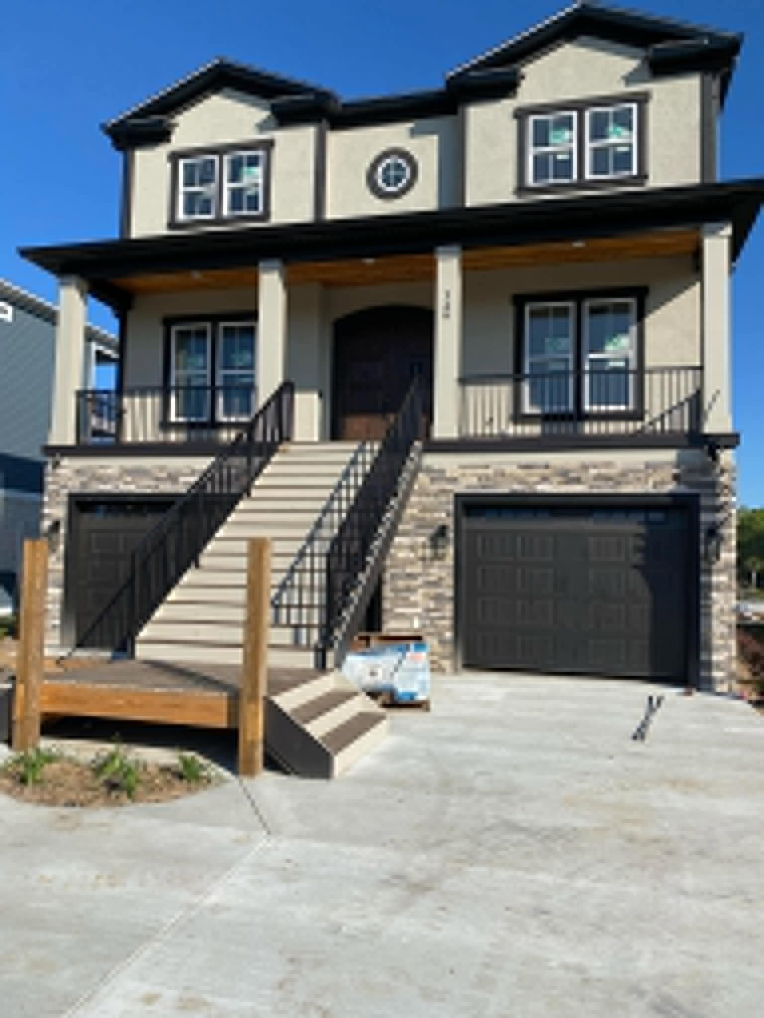 Two-story beige house with front steps, black railings, and a garage on a sloped driveway