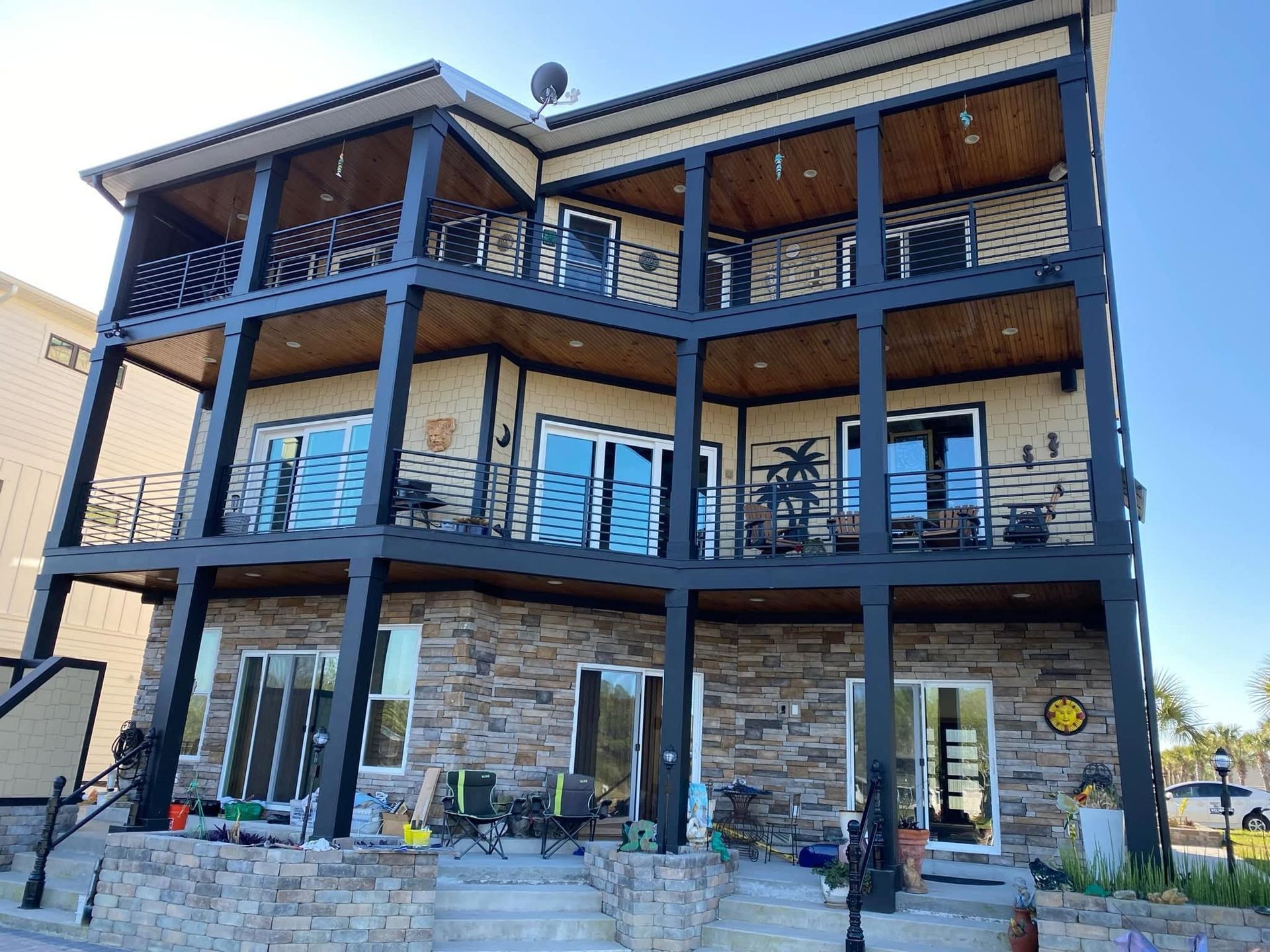 Three-story modern house with blue balconies, stone base, and large windows under a clear sky