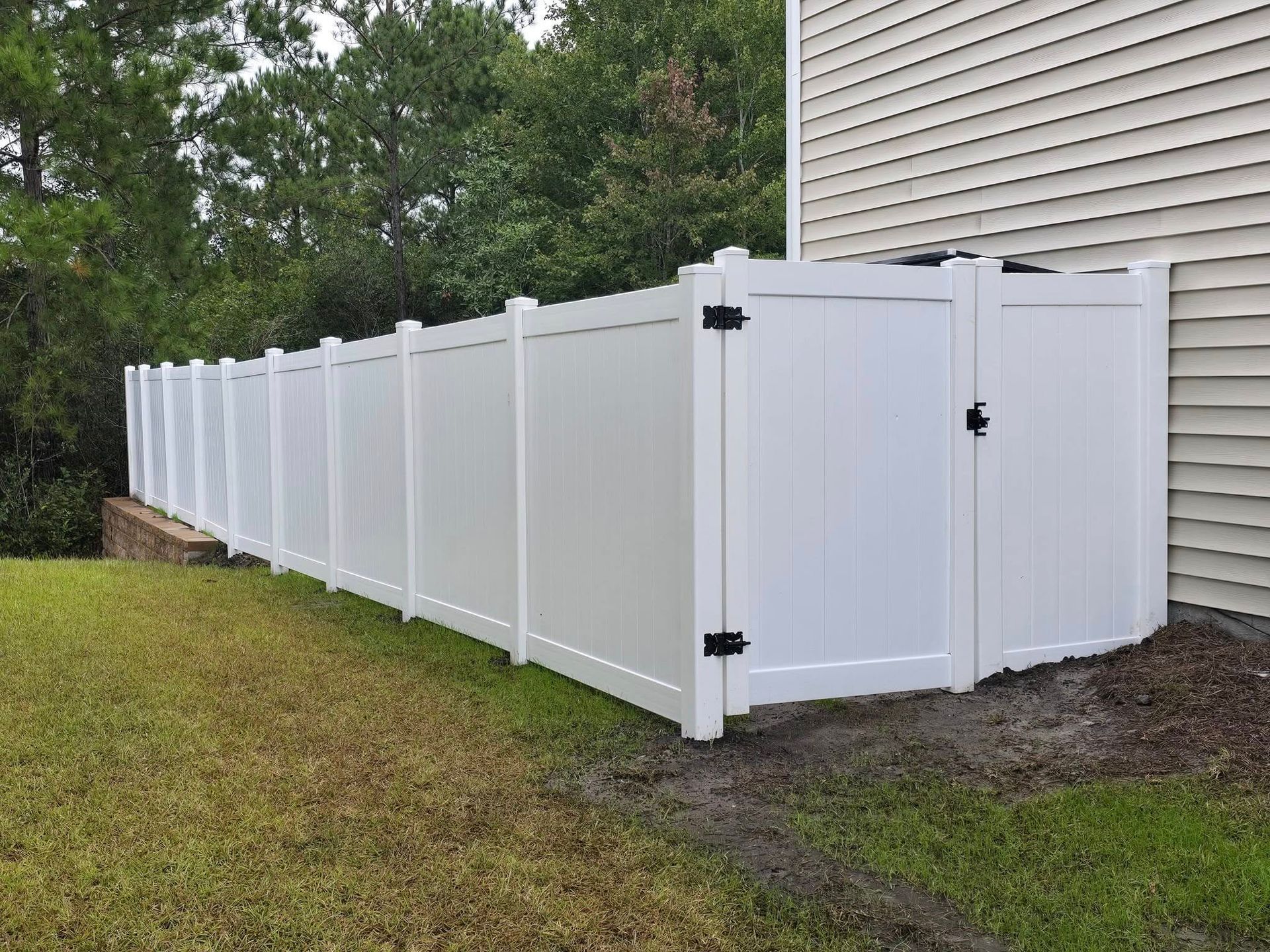 White vinyl privacy fence along a house on a grassy yard