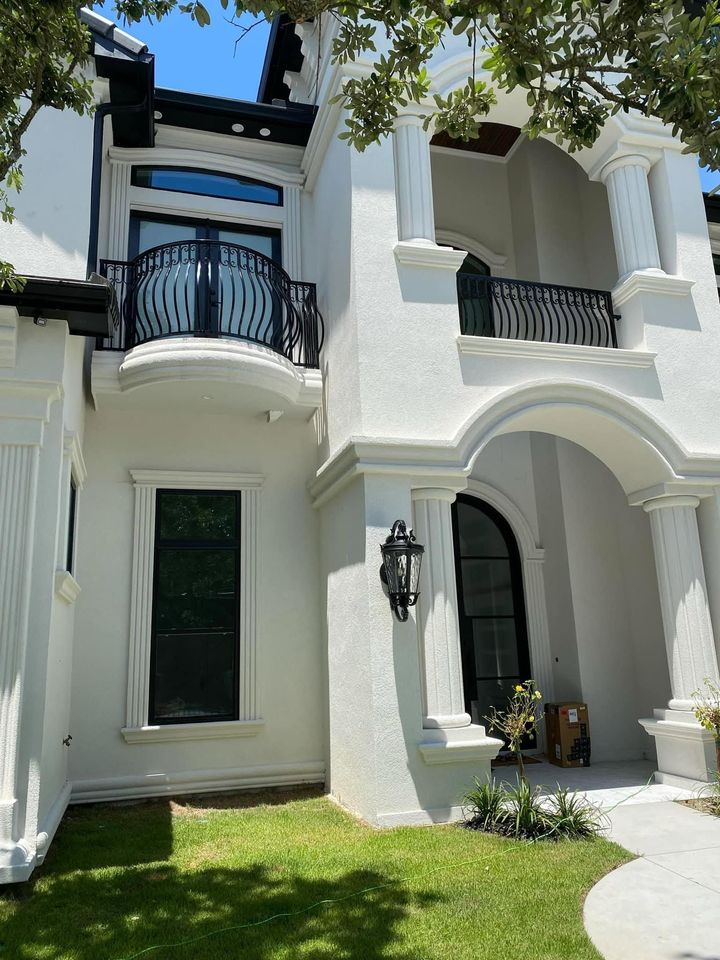 White stucco townhouse with arched balconies, black trim, and a small front lawn in bright sunlight