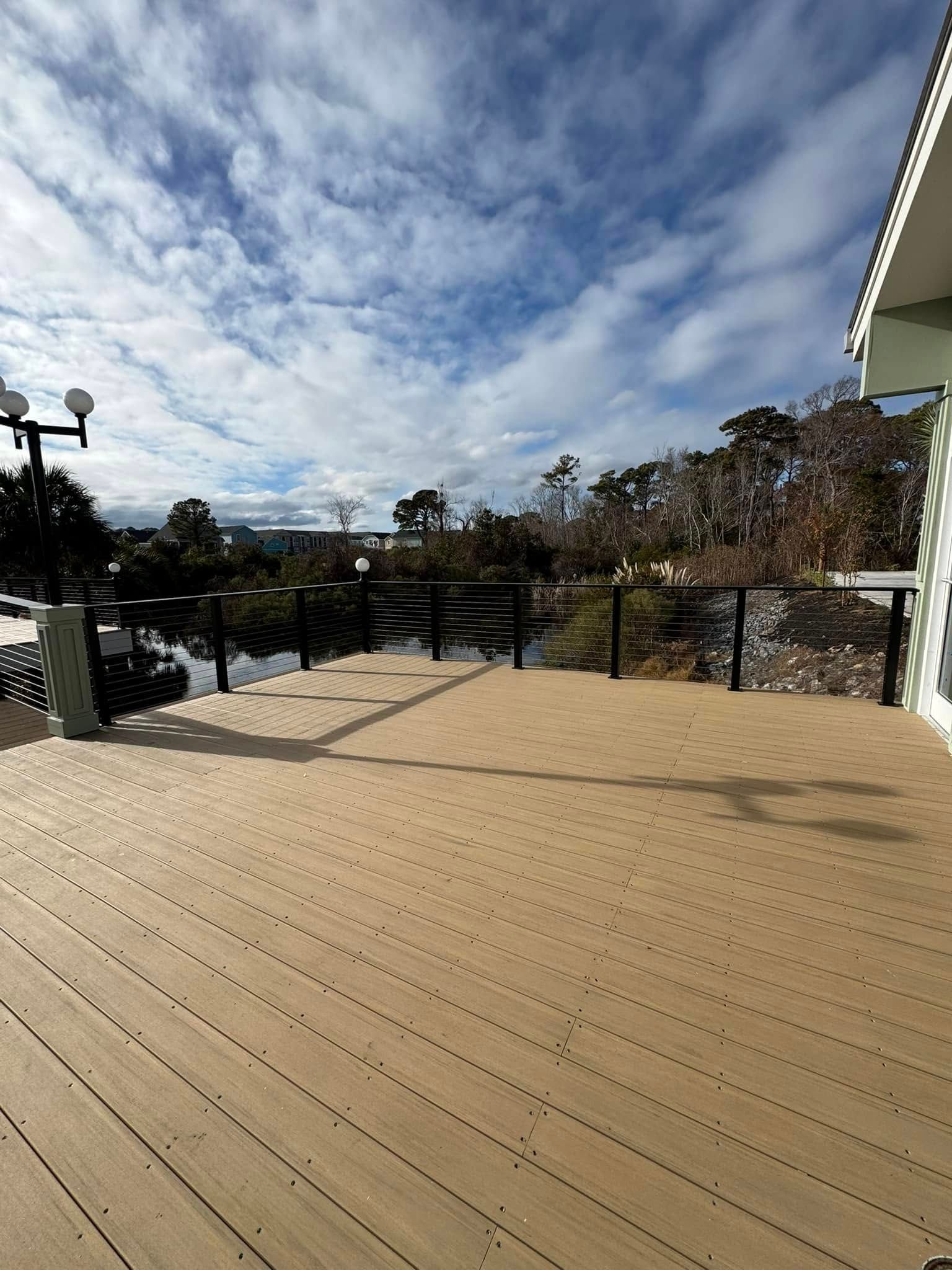 Spacious beige deck with black railing overlooking trees and cloudy sky.