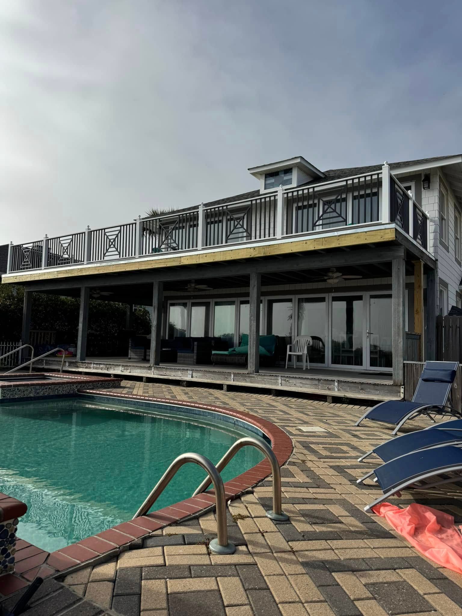 Poolside resort patio with lounge chairs, glass doors, and a turquoise swimming pool under a cloudy sky