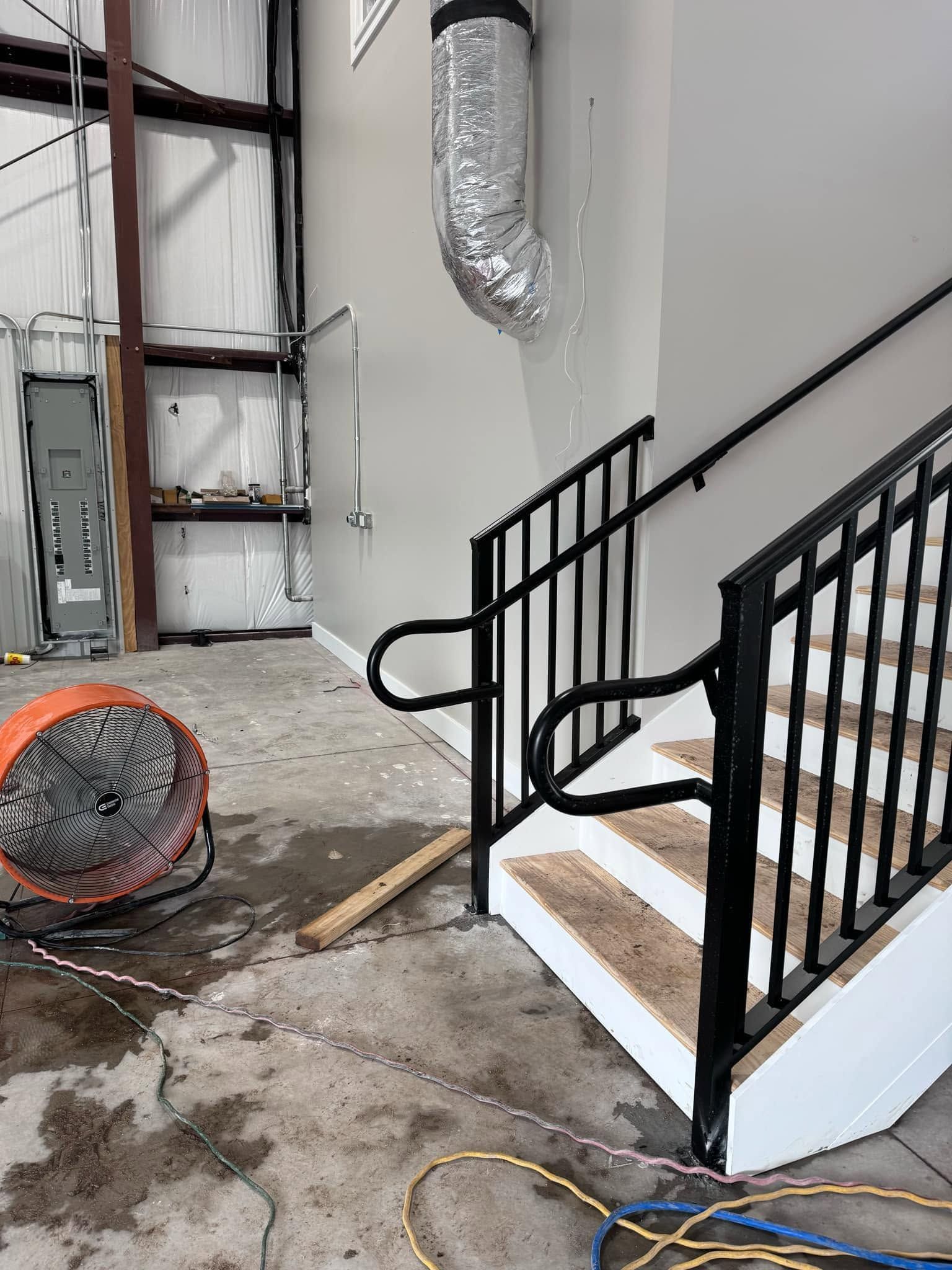 Indoor construction area with black metal stairs, exposed ductwork, and debris on the floor.