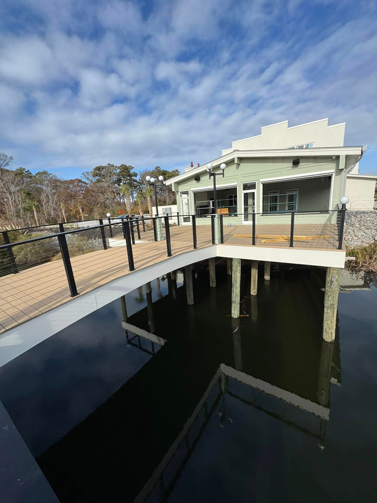 Covered dock beside a waterway, with a white building, black railings, and trees under a blue sky.