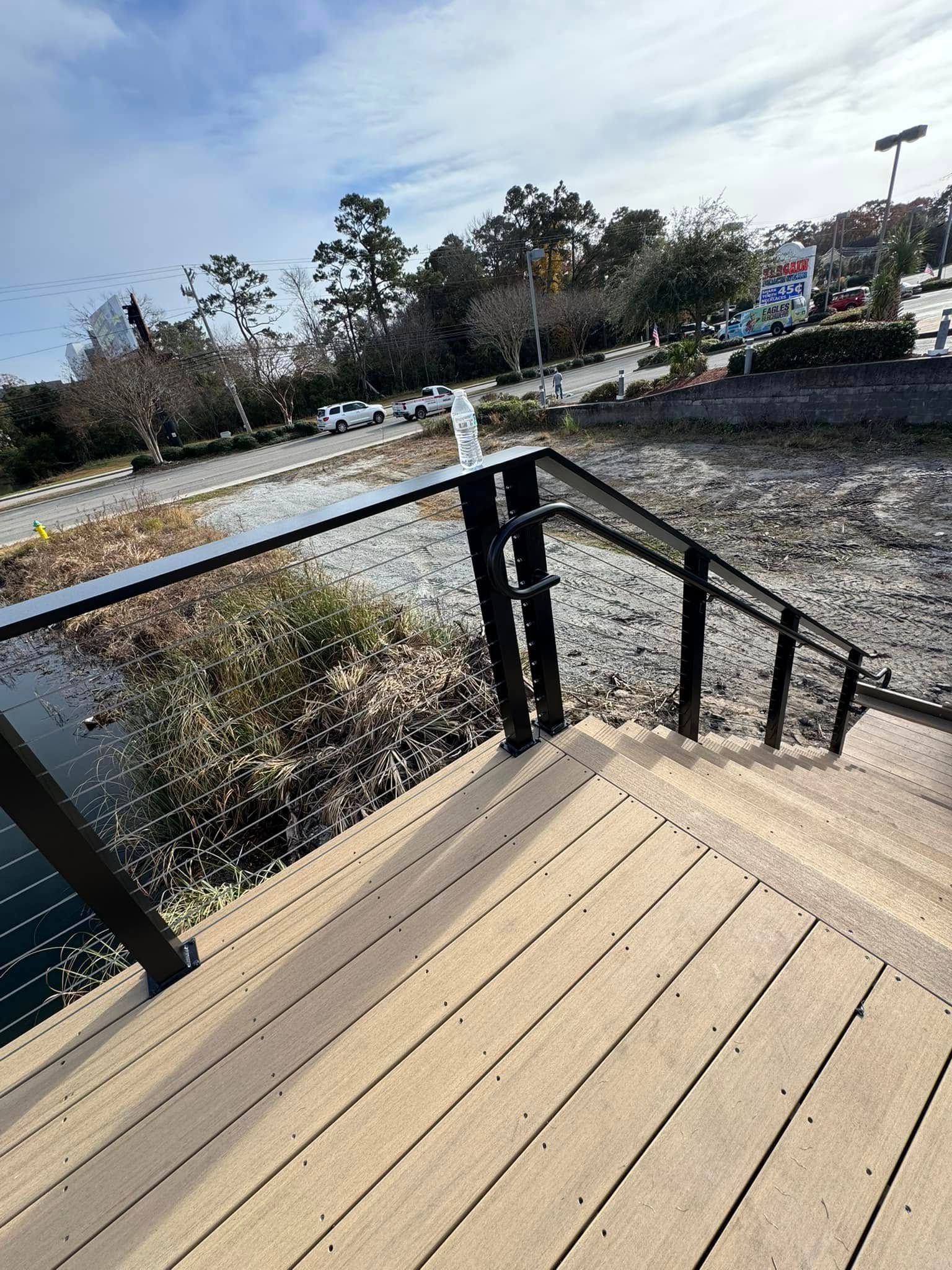 Wooden deck with black railing overlooking a river and trees on a sunny day