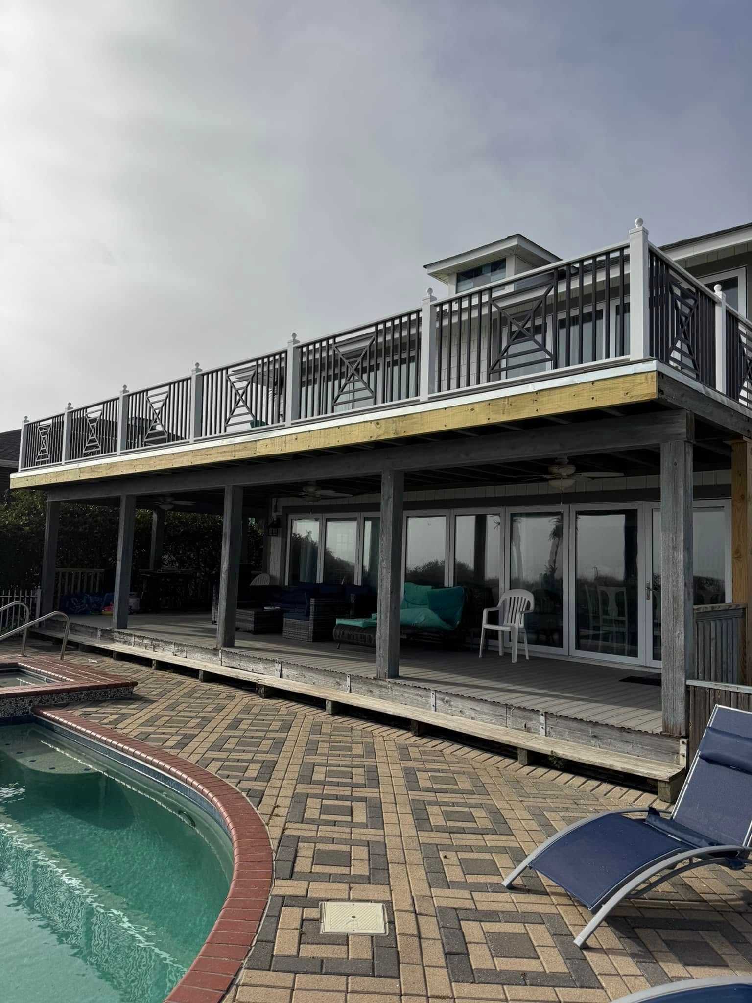 Poolside patio with tiled deck, lounge chair, and glass-front modern house under an overcast sky