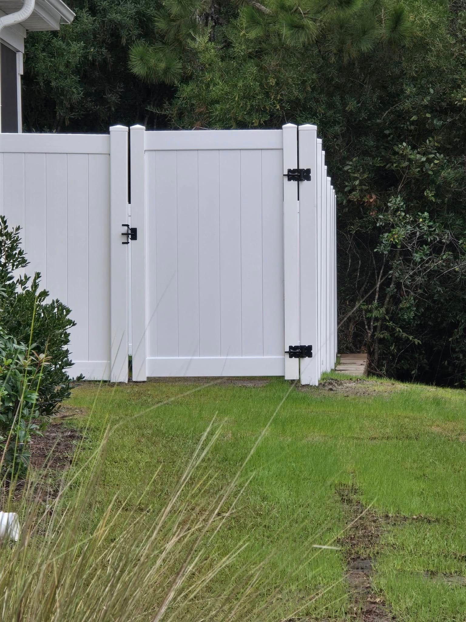 White wooden garden gate with black hinges beside a grassy lawn and greenery.