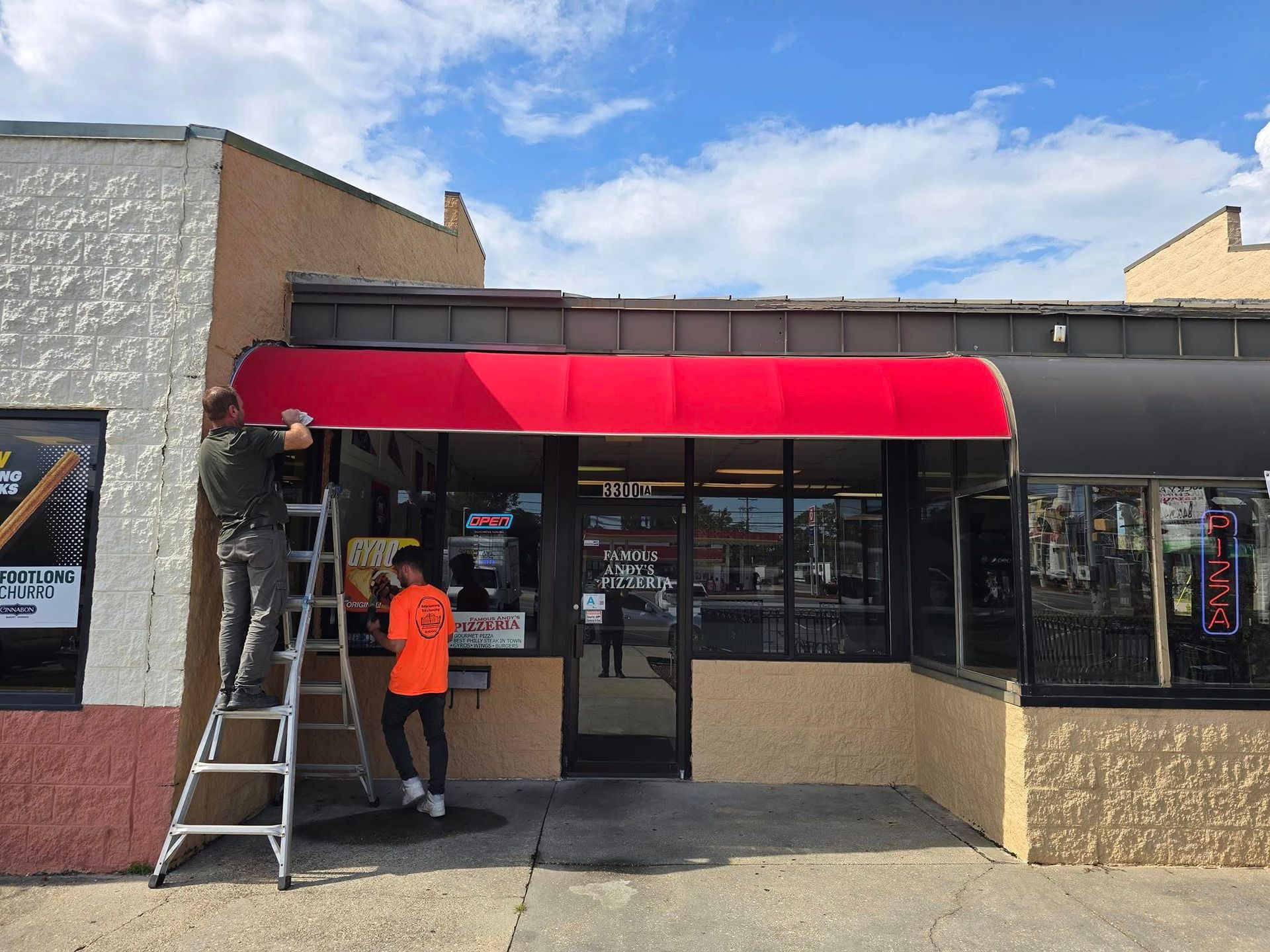 Person on ladder working on red awning outside a storefront.