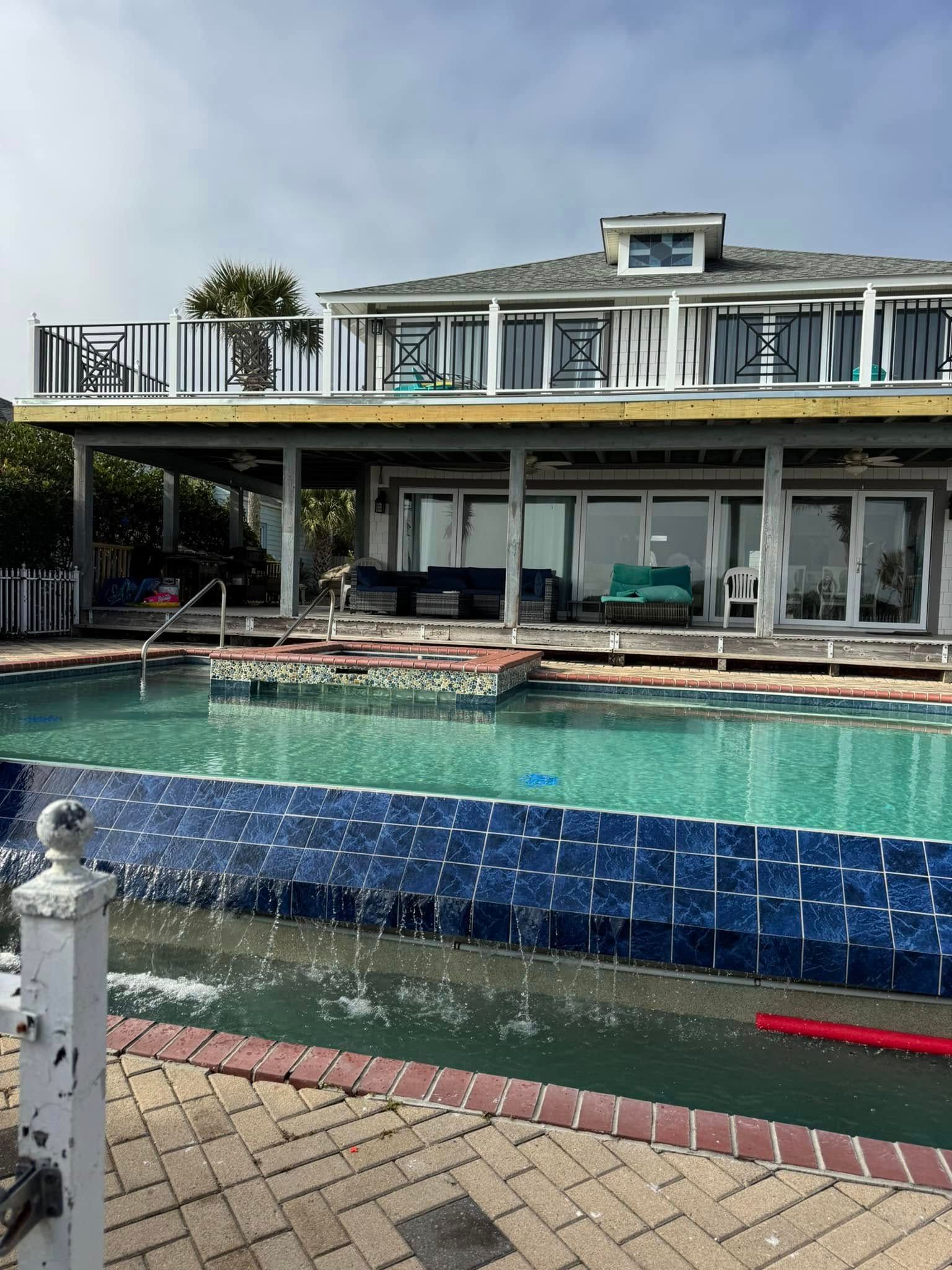 Backyard pool with two-story house and patio seating under a partly cloudy sky