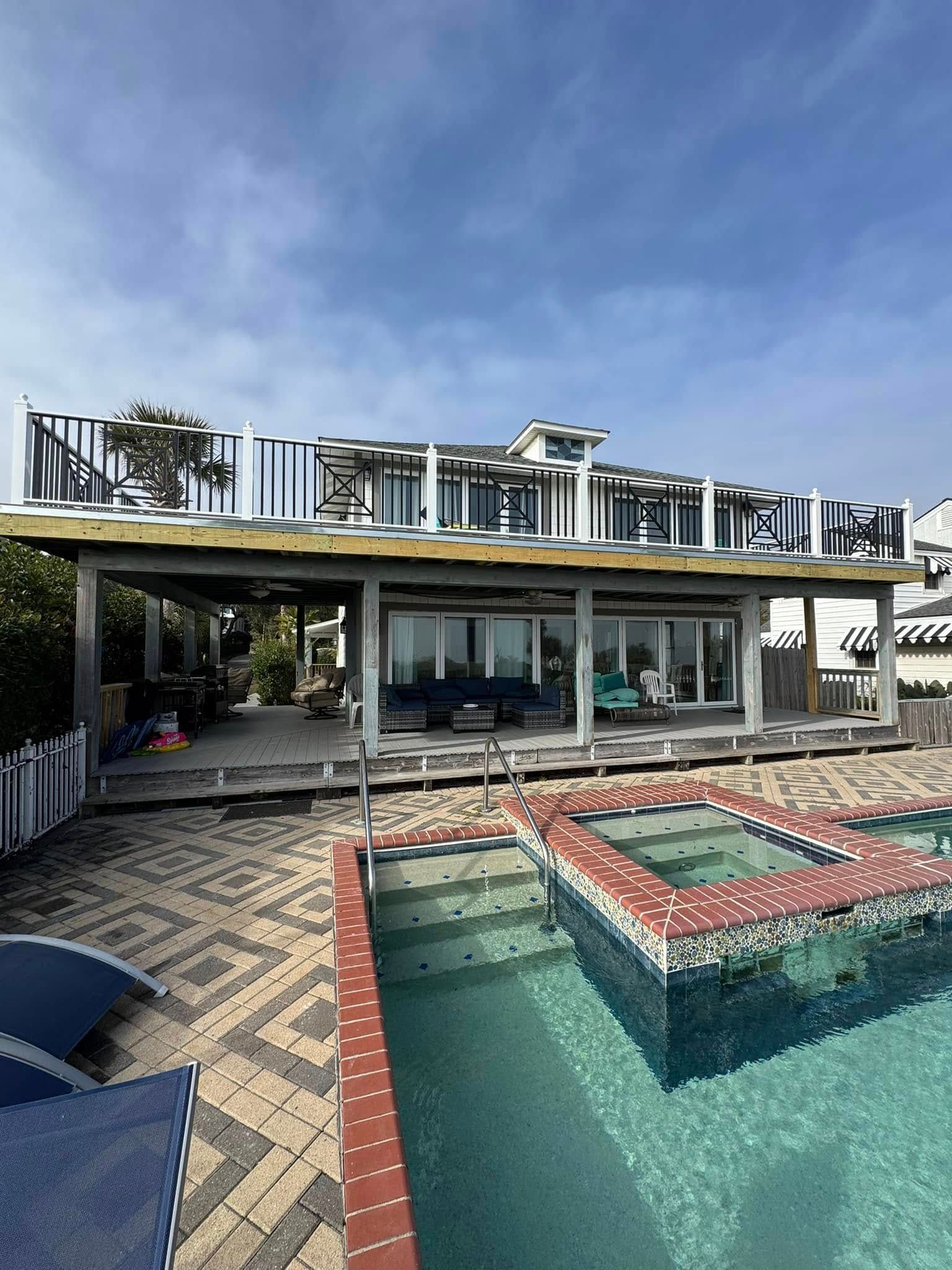 Backyard pool with turquoise water, red-tiled spa, patio seating, and a modern house under a blue sky