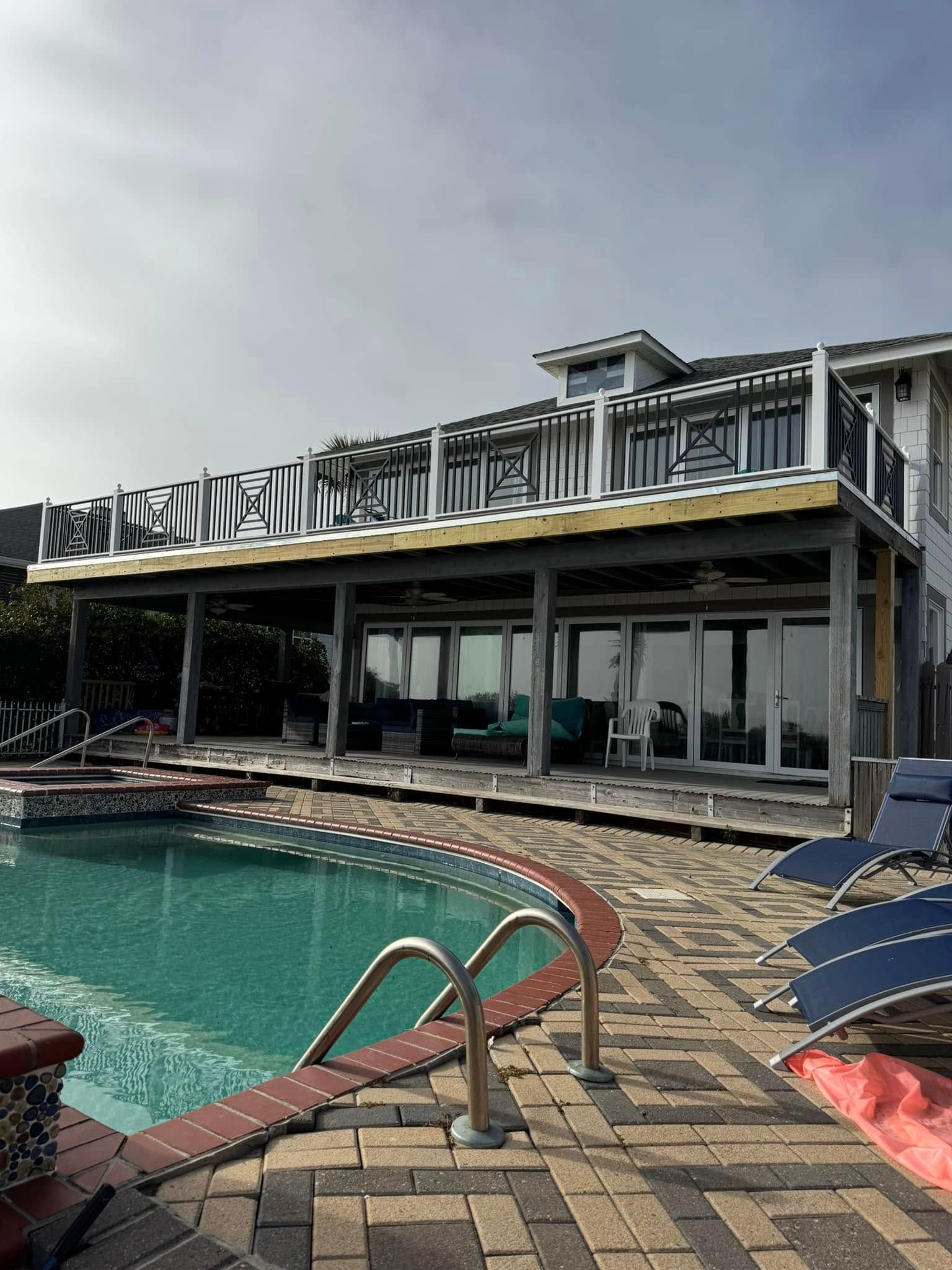 Poolside resort building with turquoise water, lounge chairs, and cloudy sky