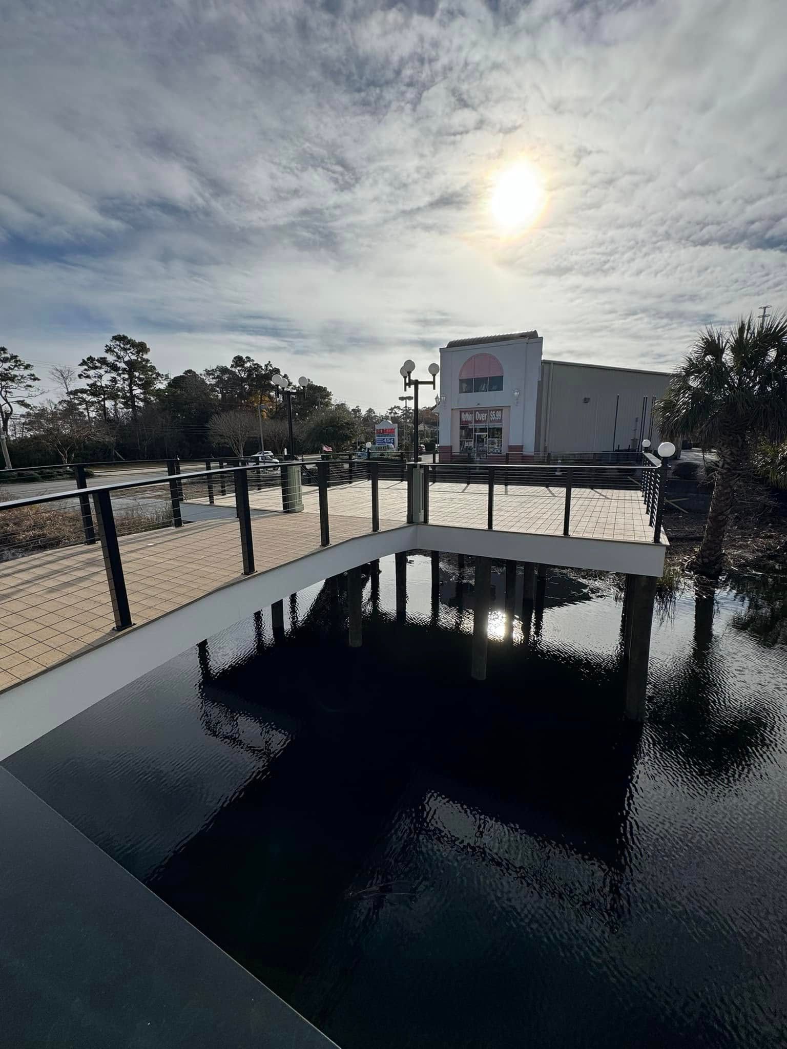 Outdoor pool with dark water beside a white building under a bright cloudy sky