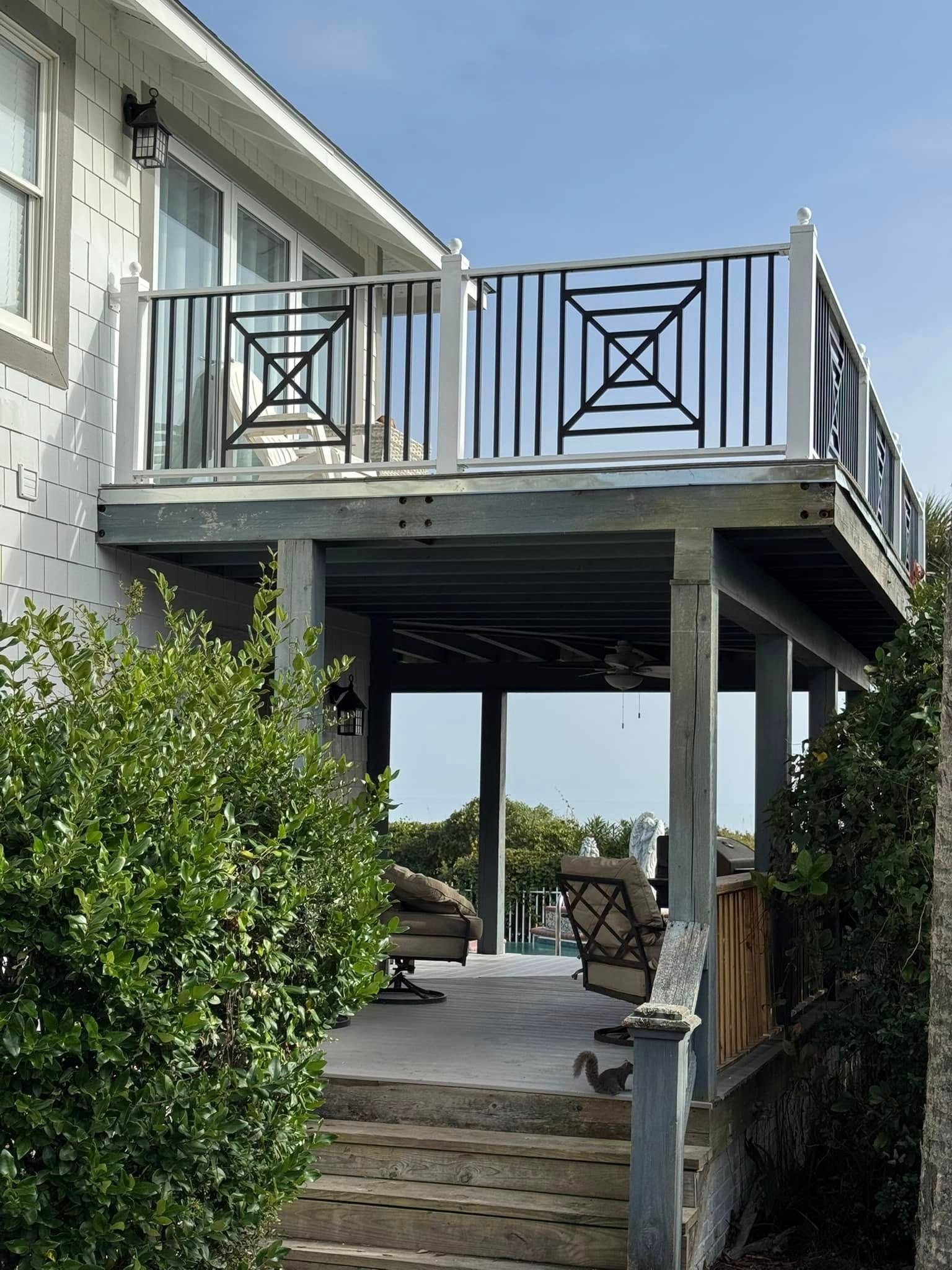 Back deck with black railings and stairs beside a house, overlooking a yard with bushes and patio furniture