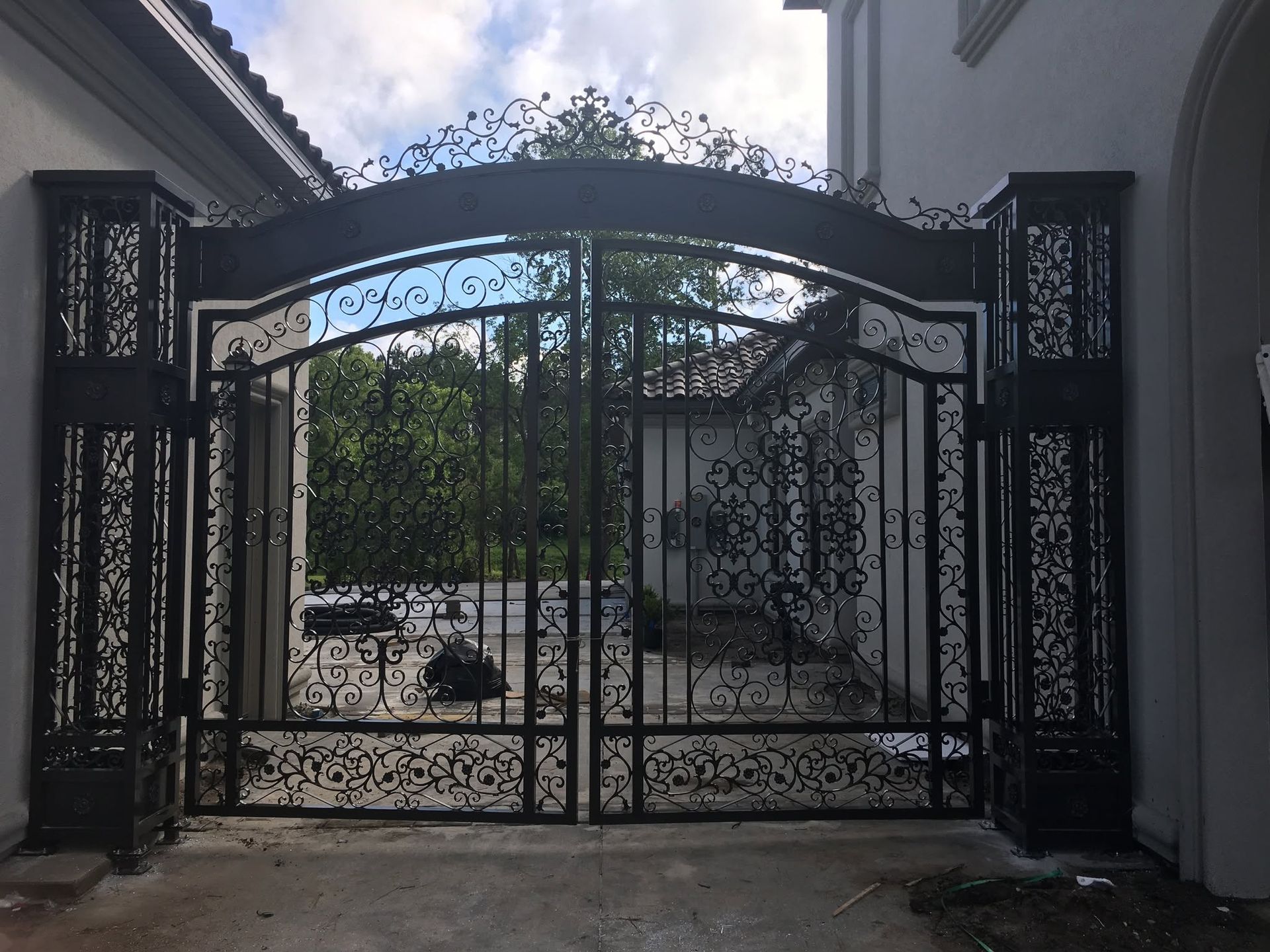 Black wrought-iron gate at the entrance of a driveway between white buildings.