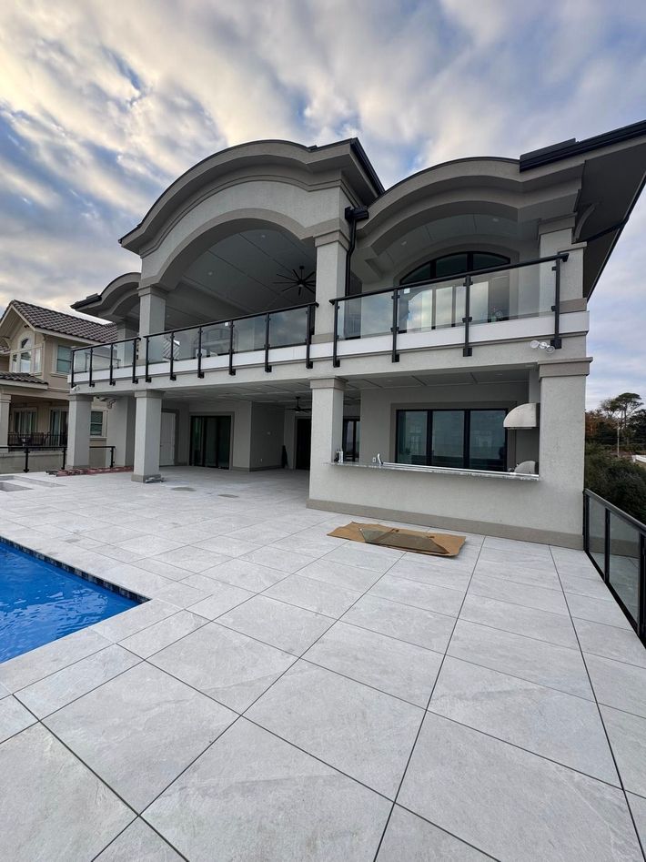 Modern white two-story house with arched balcony, glass railing, and poolside patio at sunset