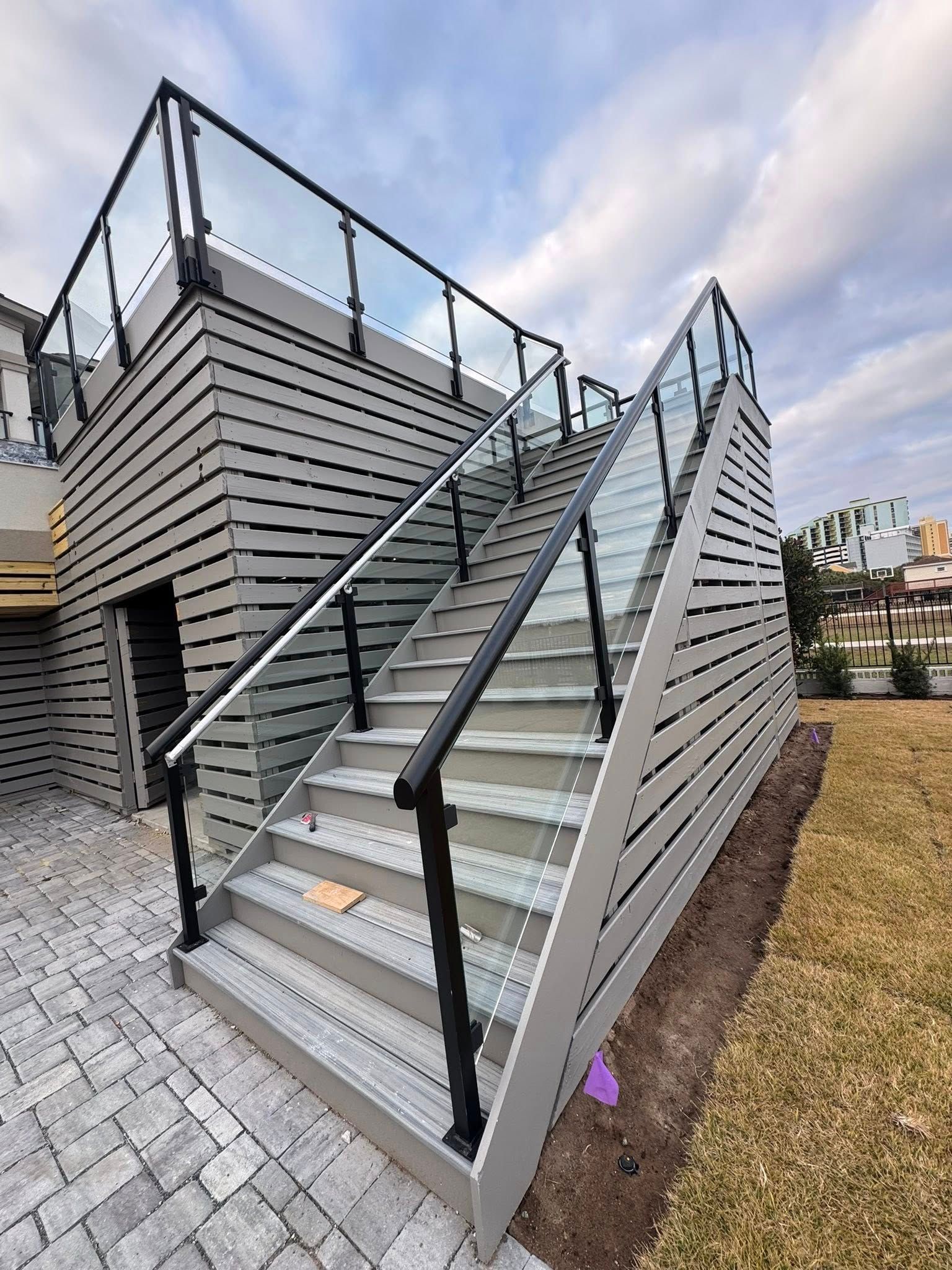 Outdoor metal staircase with gray railings beside a modern striped building under a cloudy sky