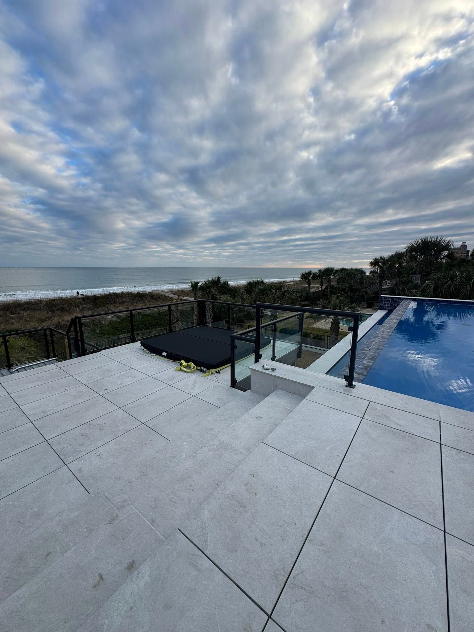 Oceanfront patio with white tiles, pool, and cloudy sky overlooking the sea