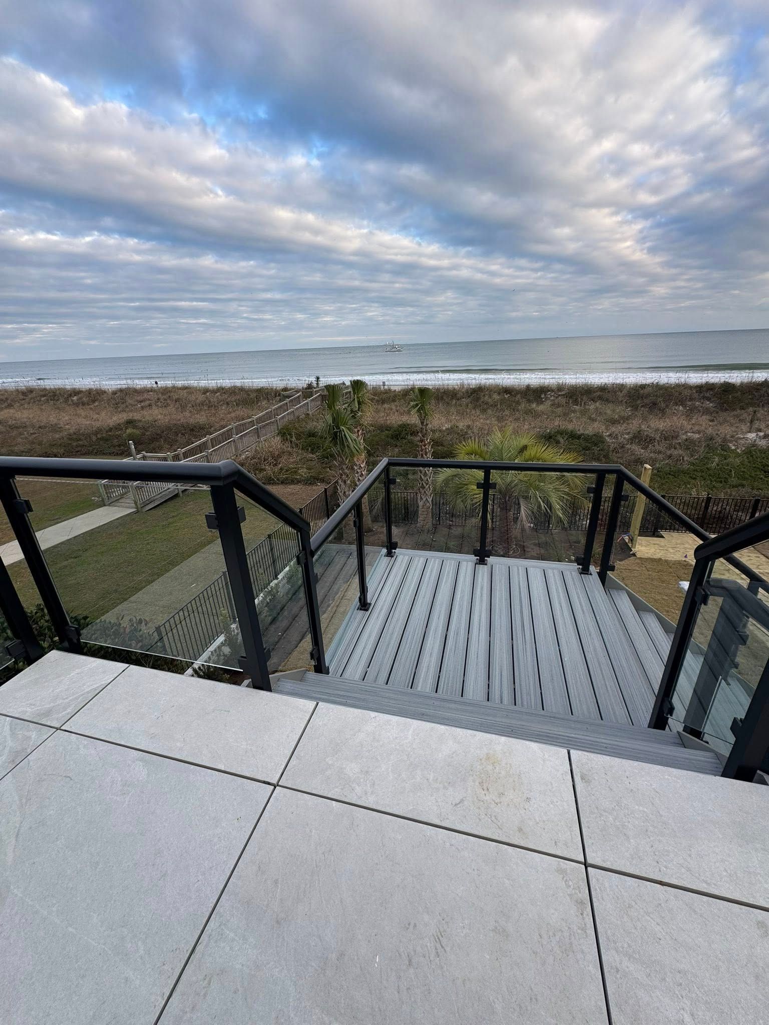 Boardwalk steps to a beach with black railings, ocean waves, and a cloudy sky.