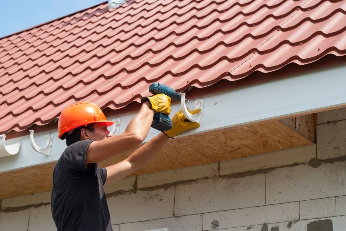 Worker using a yellow power saw to cut roof eaves under a red tile roof