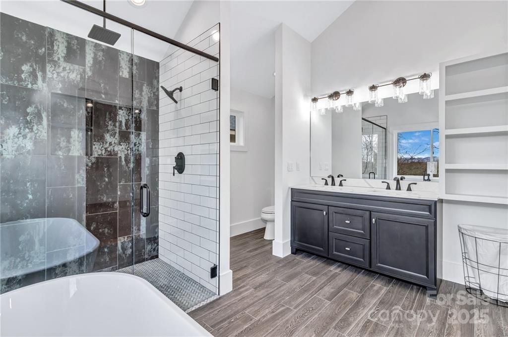 Modern bathroom with dark gray vanity, glass shower, and patterned tile.