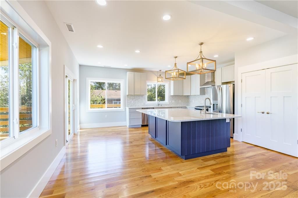 Bright open kitchen with blue island, white cabinets, stainless appliances, and large windows