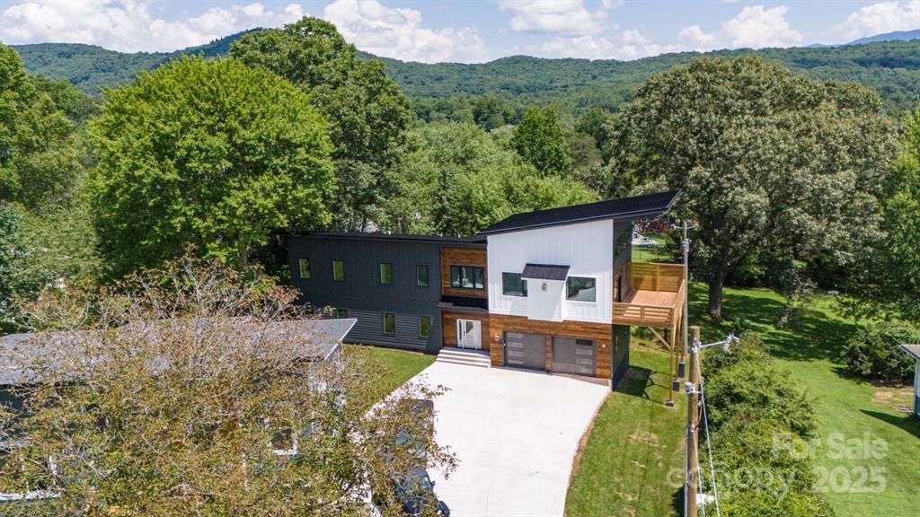 Modern house with black and white exterior, attached garage, and deck, nestled in a tree-filled mountain setting.