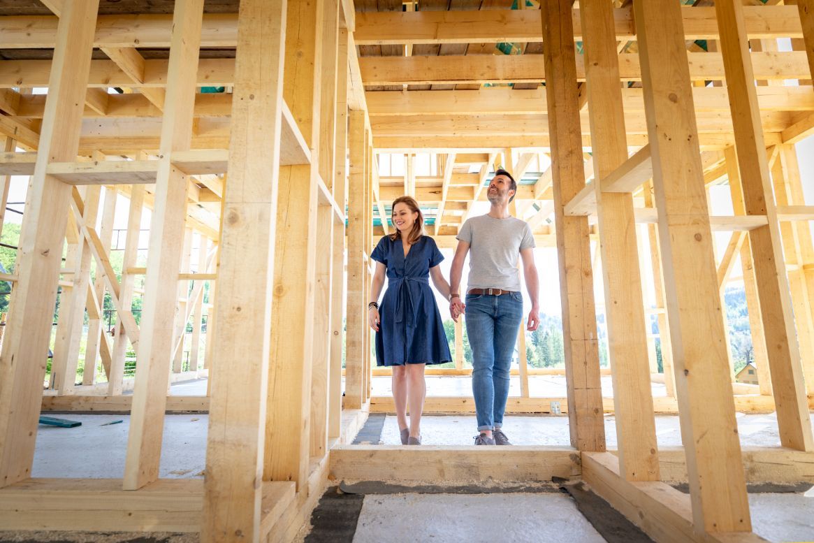 Couple holding hands, standing in the wooden frame of a house under construction.