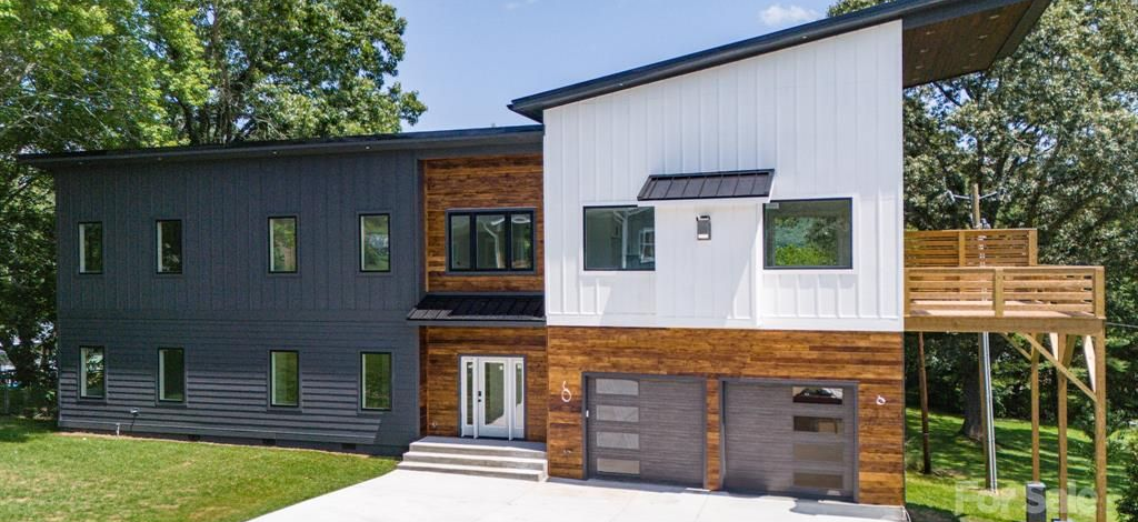 Modern two-story house with dark gray and white siding, wood accents, and a front lawn
