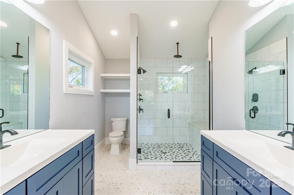 Bright modern bathroom with double vanities and a glass-enclosed shower.
