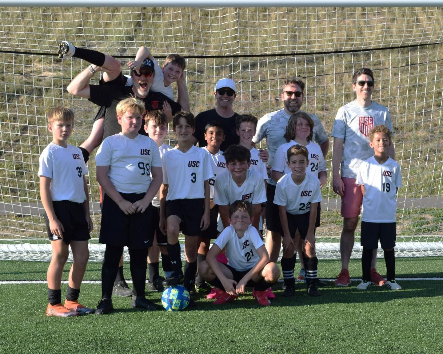 Youth soccer team posing on a field with a coach and goal net in the background
