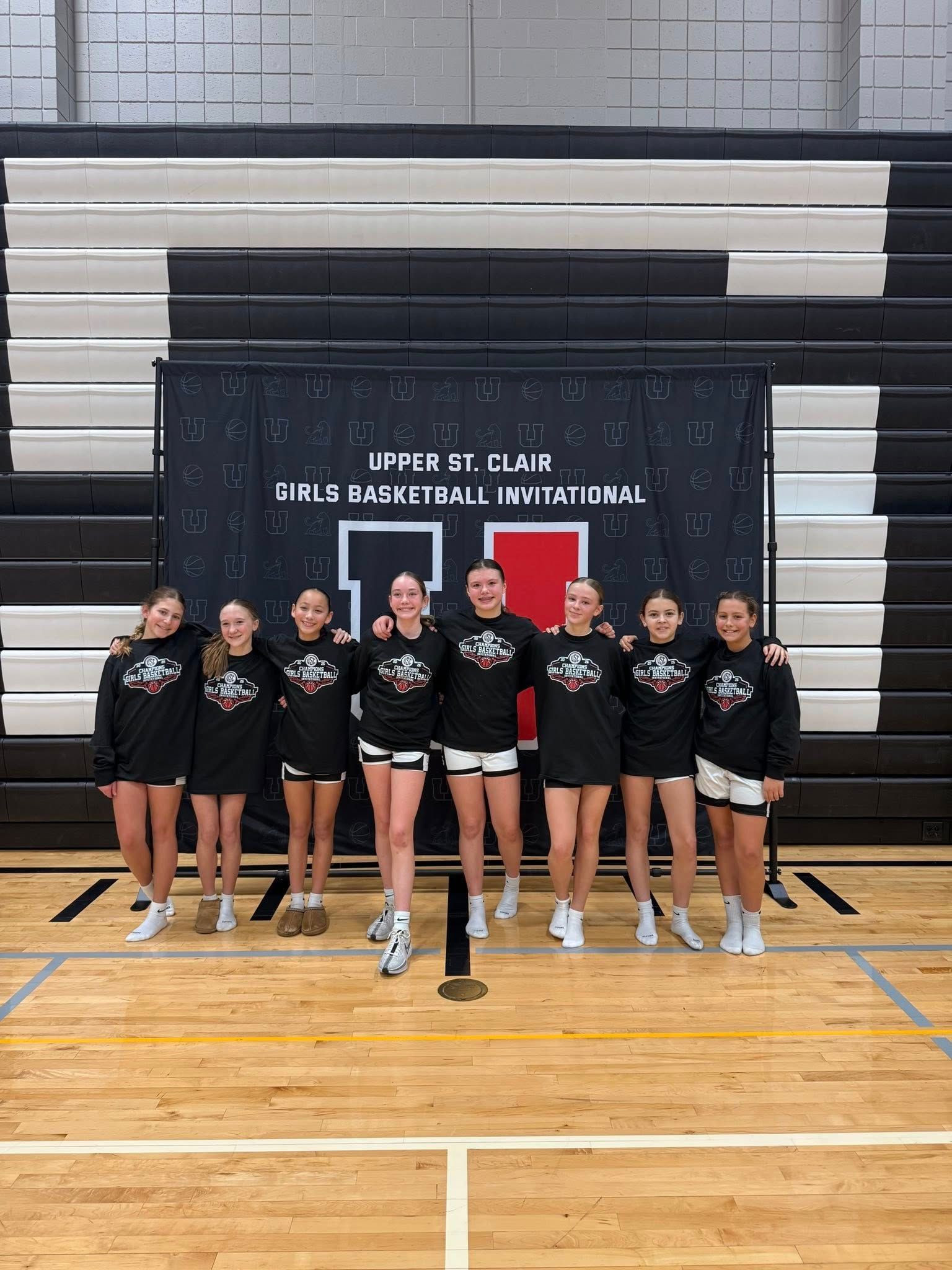 Cheer team posing in a gym in front of a black sign and white-and-black wall padding