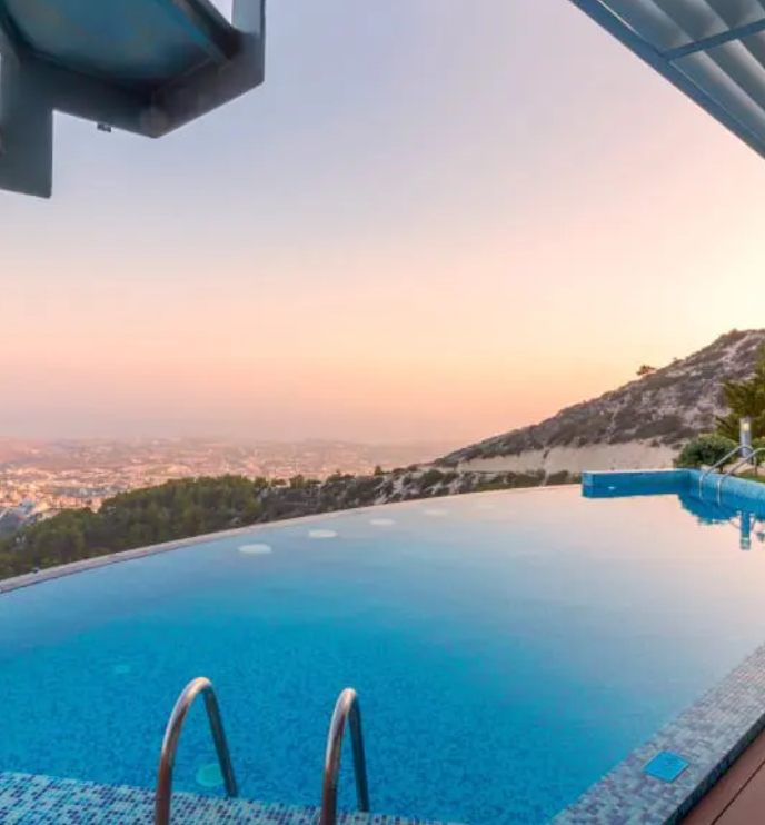 Infinity pool overlooking a city at sunset, with blue water and a hillside backdrop