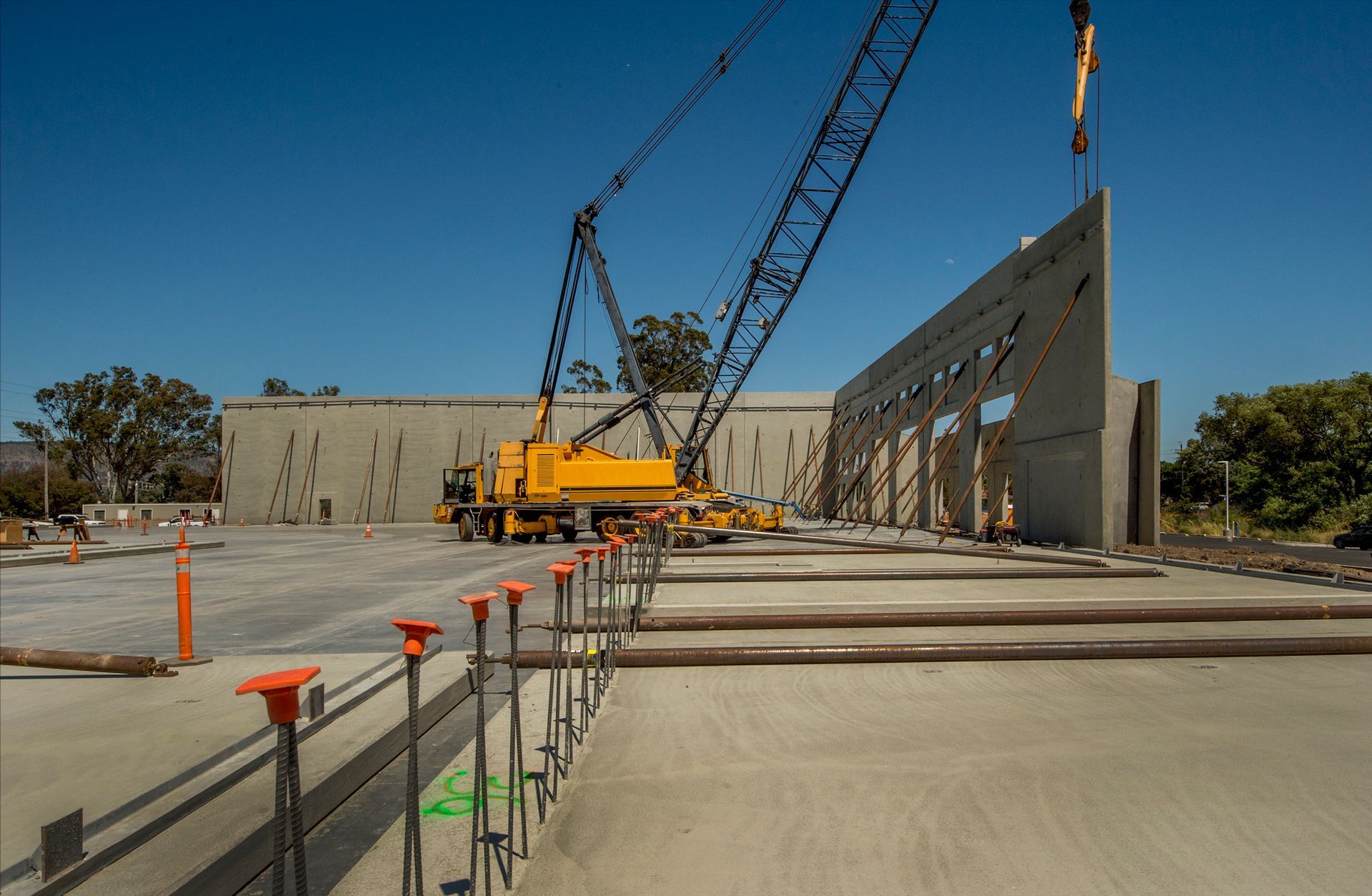 A yellow crane lifting a concrete wall panel at a construction site on a sunny day.