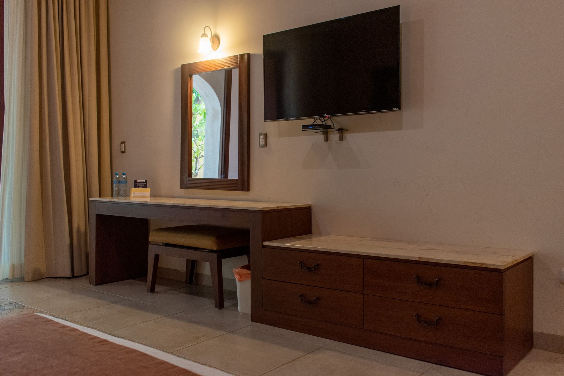 Una habitación de hotel con escritorio, tocador, televisión y espejo.
