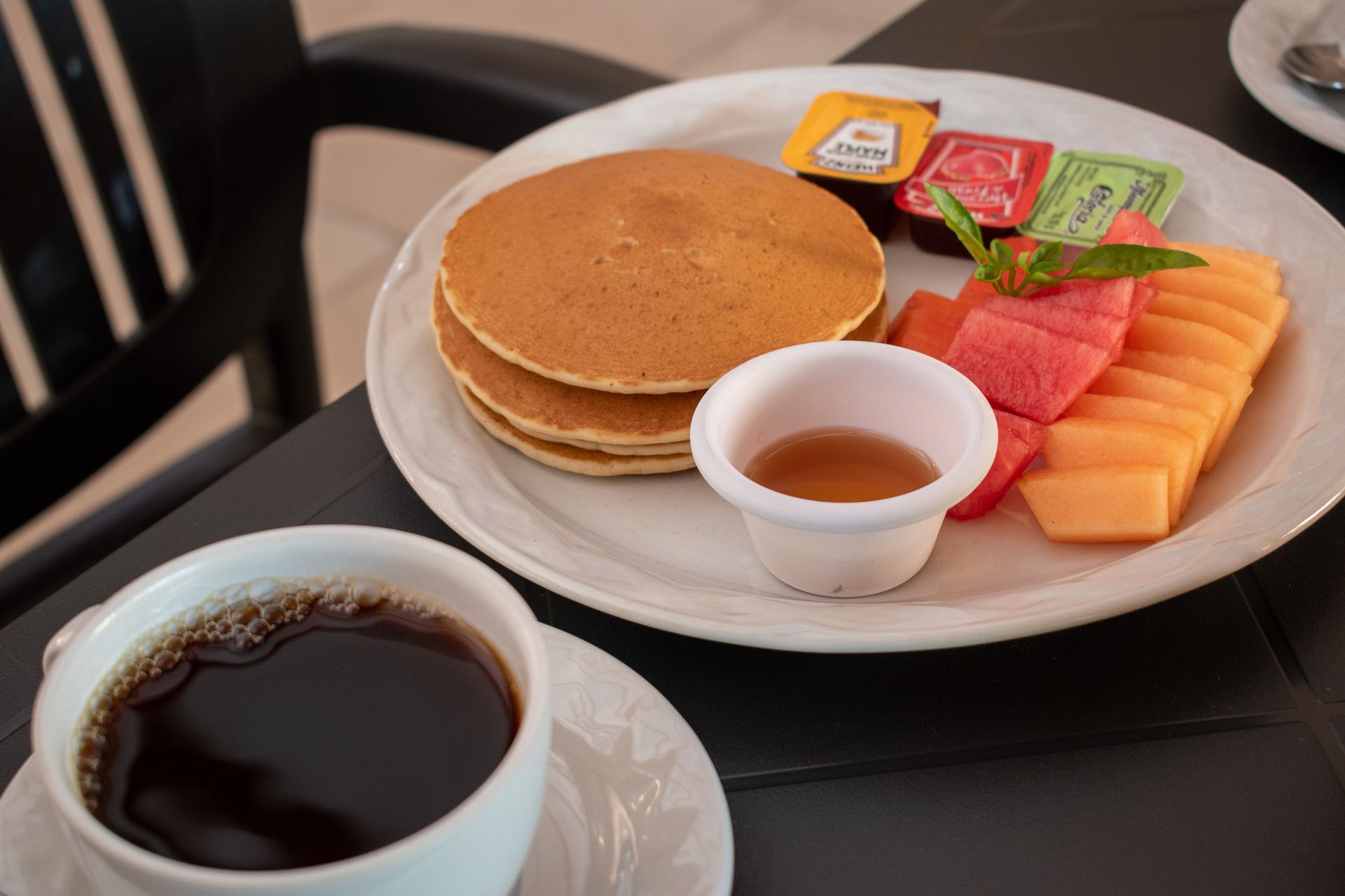 Un plato de panqueques, fruta y una taza de café sobre una mesa.