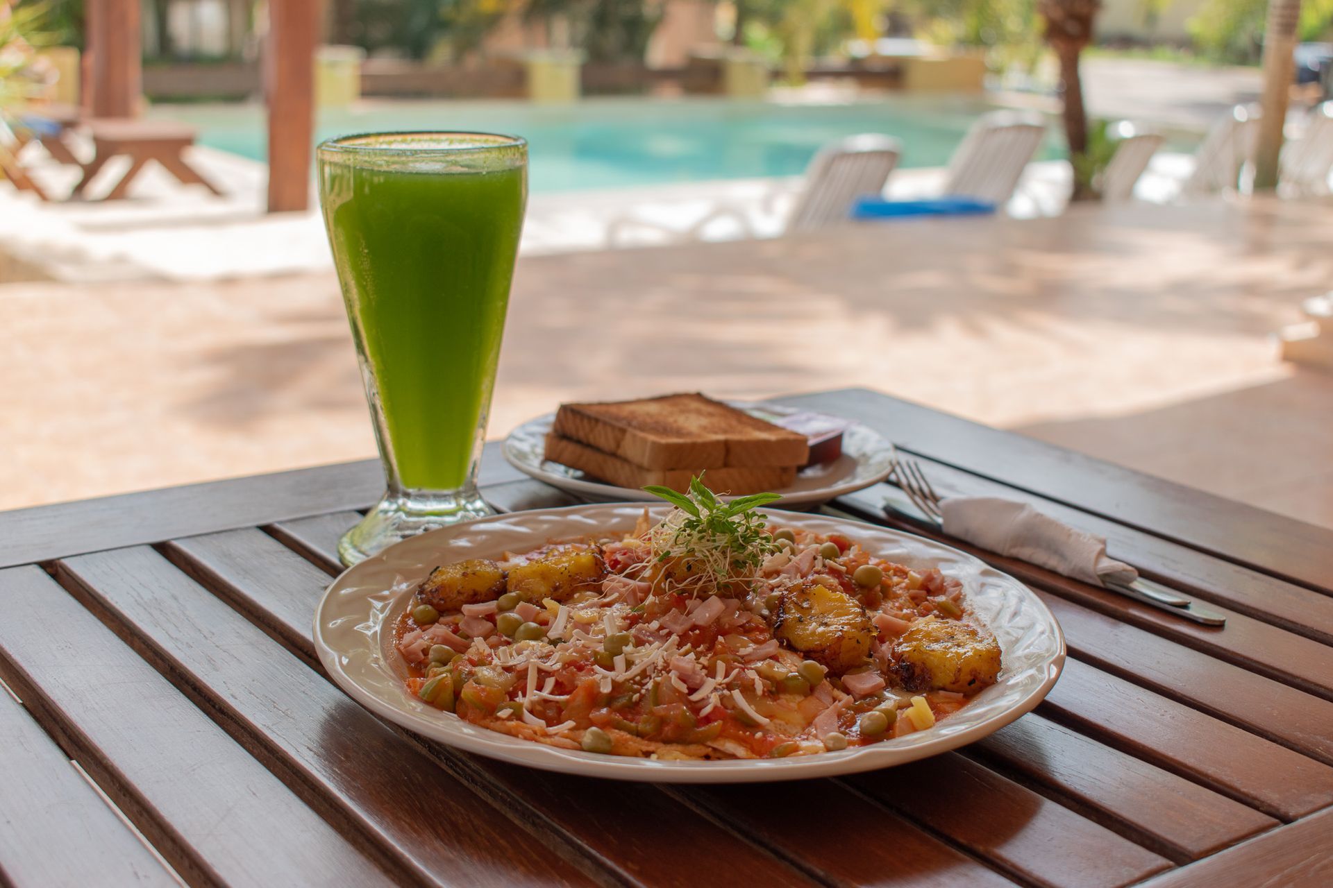 Un plato de comida y un vaso de jugo verde sobre una mesa de madera.