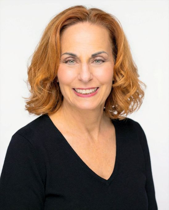 Smiling woman with shoulder-length auburn hair wearing a black top against a white background