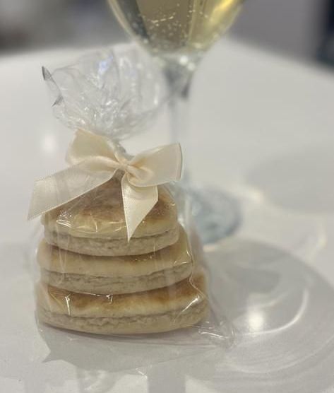 Bakestone Wales | A stack of pancakes wrapped in plastic with a bow on a table next to a glass of wine.